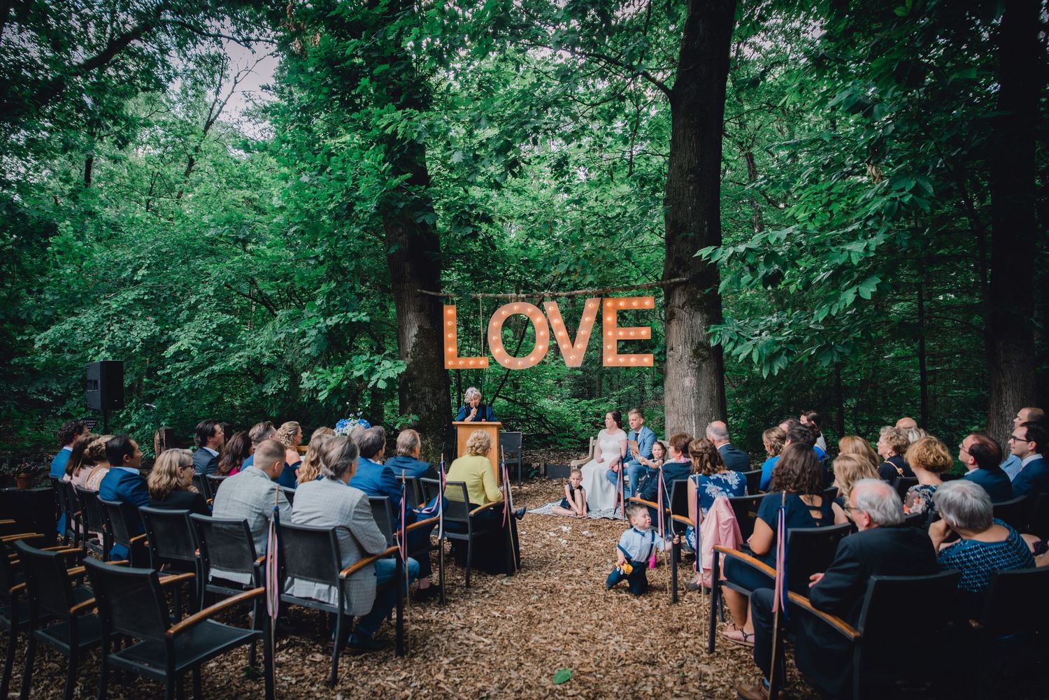 Buiten ceremonie in bos met lichtjes en LOVE letters, sfeervolle bruidsfotografie bij Mr van Eijck Oisterwijk, Brabant.