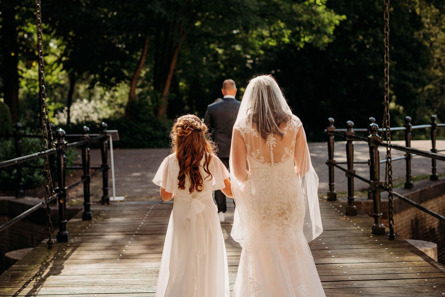 Wedding party walking along a tree-lined pathway with dappled sunlight.
