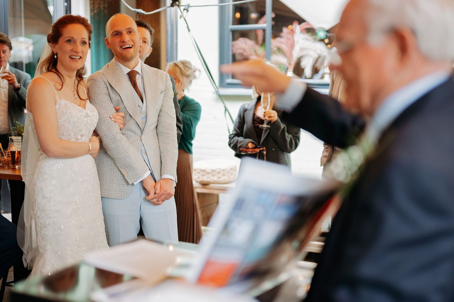 Bride and groom smiling together during wedding reception while guest reads a book.