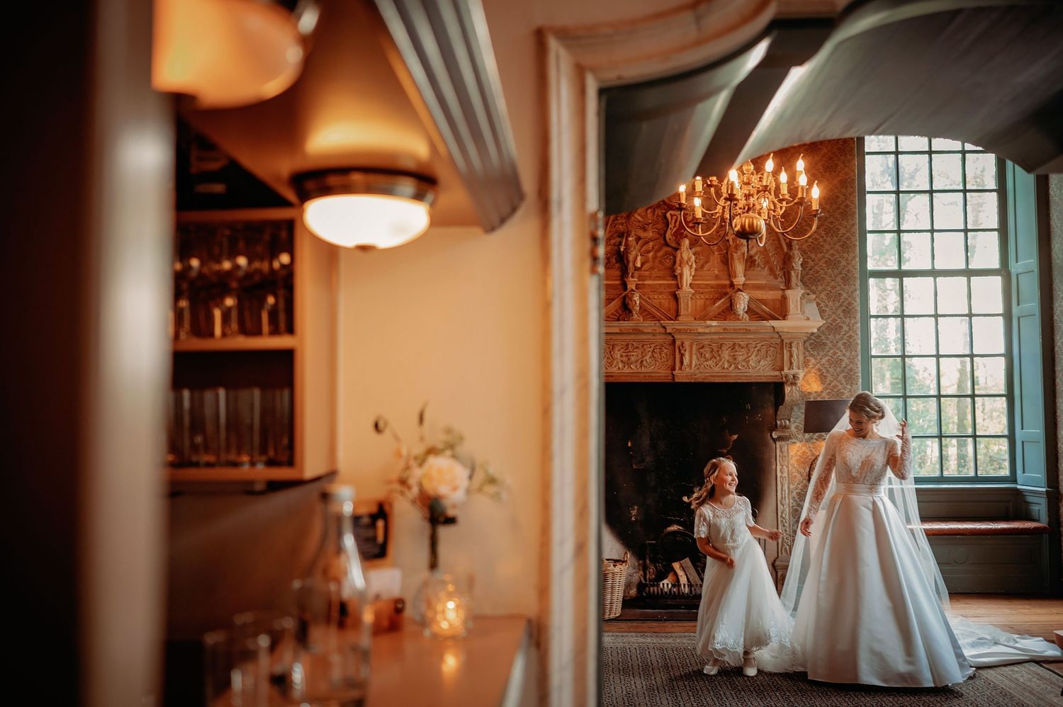 Bruidspaar in elegante zaal met kroonluchters en raamlicht, romantische bruidsfotografie bij Kasteel Wijenburg Echteld, Brabant.