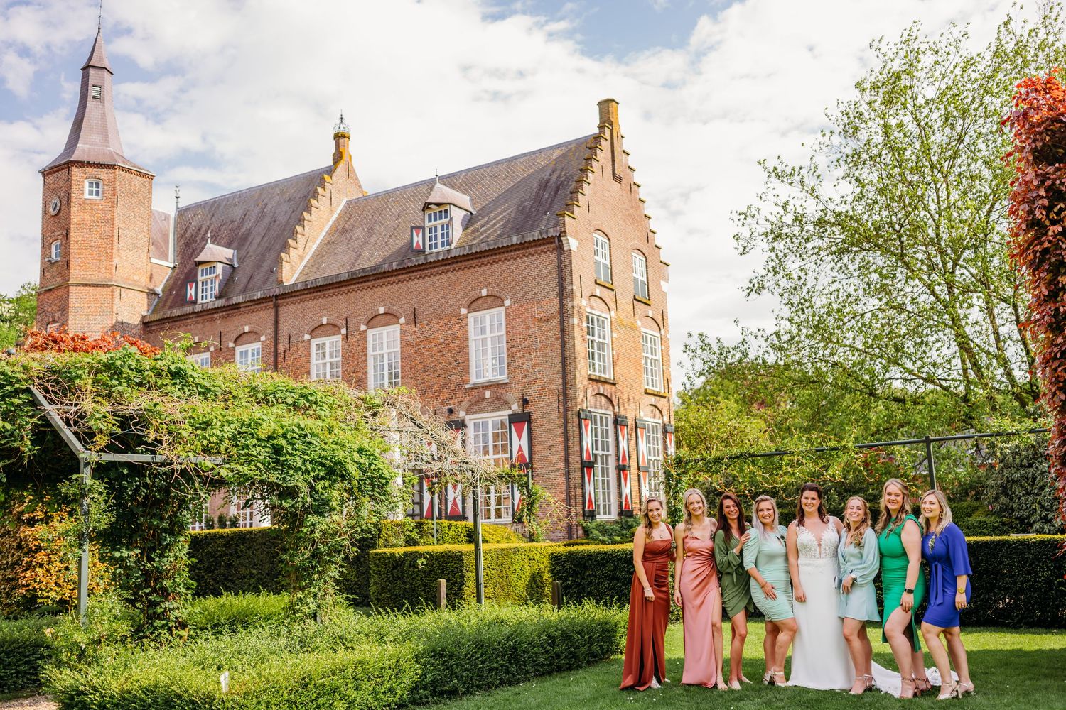 Groepsfoto van bruiloftsgasten voor groot bakstenen pand met tuin, bruidsfotografie Kasteel Maurick Vught, Brabant.