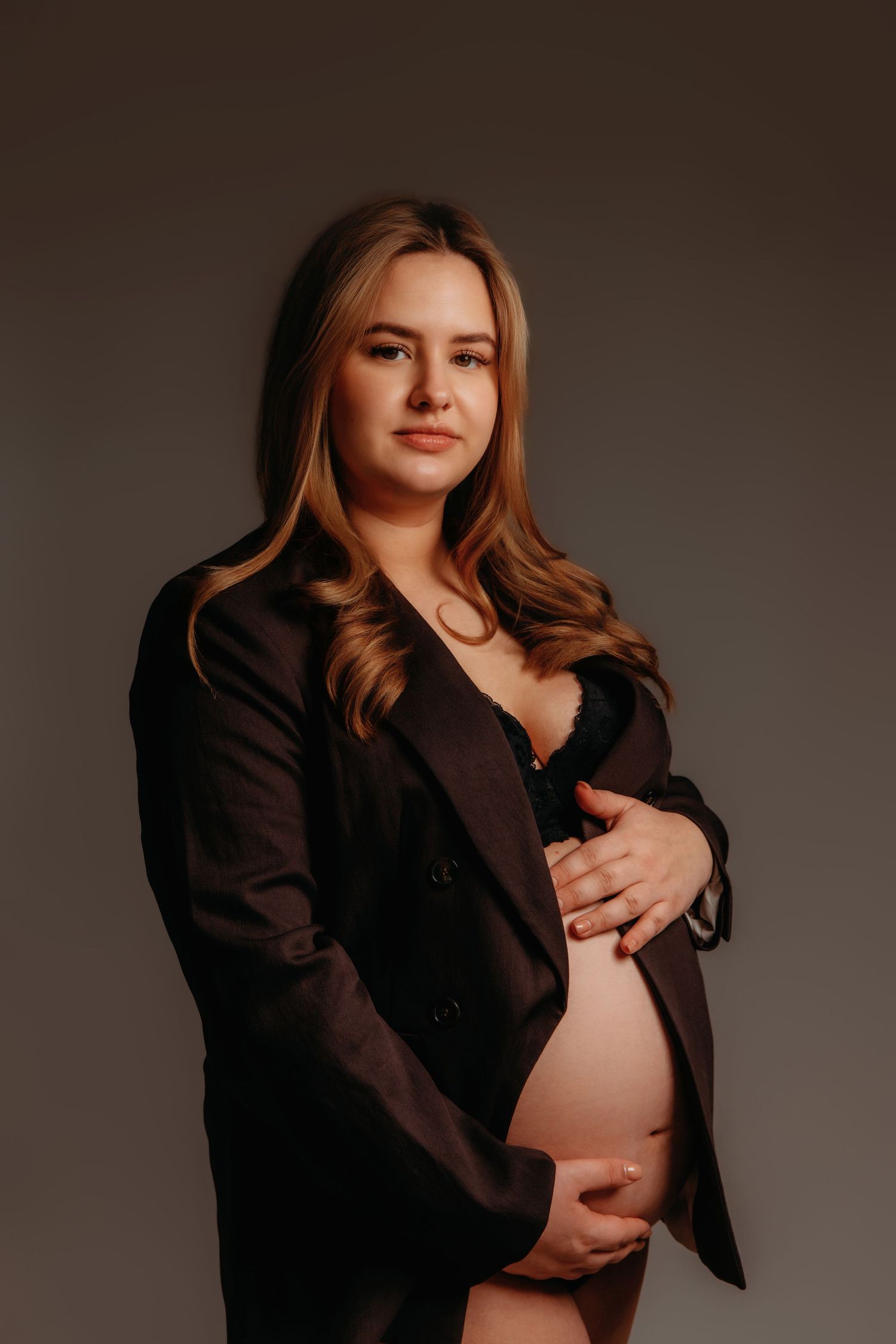 Zwangerschapsportret van vrouw in zwarte blazer die haar buik omhelst, zwangerschapsfotografie Brabant