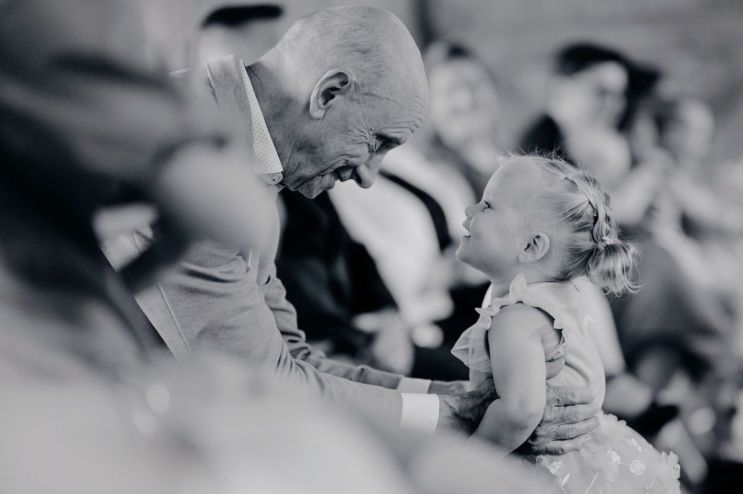 Tender black and white moment between a bald man and a curly-haired toddler girl at a wedding ceremony.