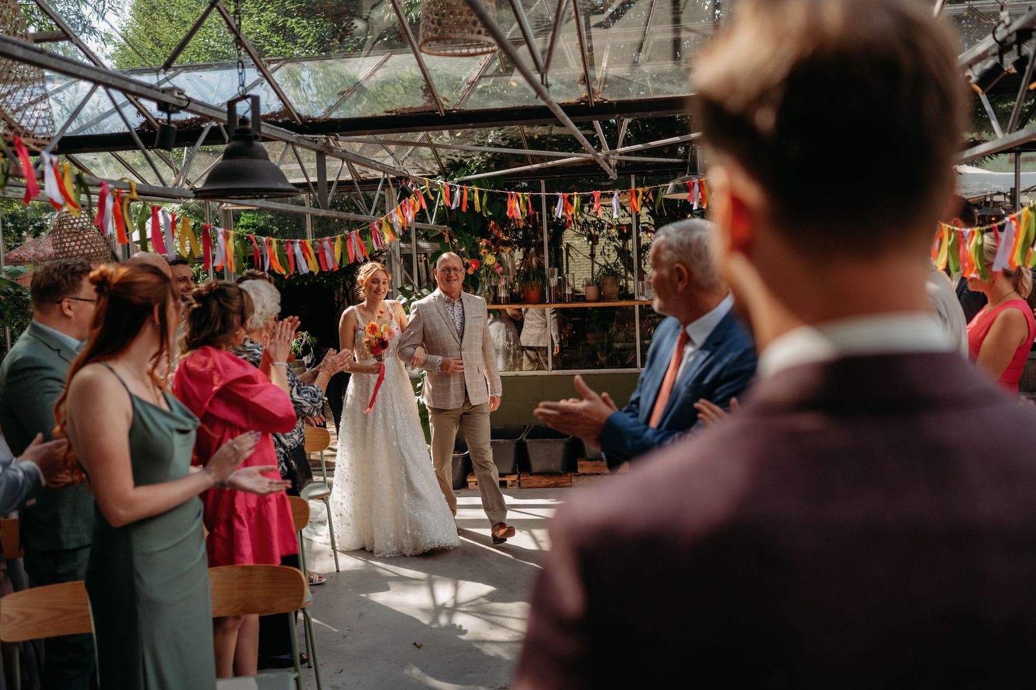 Bruiloft ceremonie met gasten onder lichtslingers en groen decor in kas, bruidsfotograaf Vught