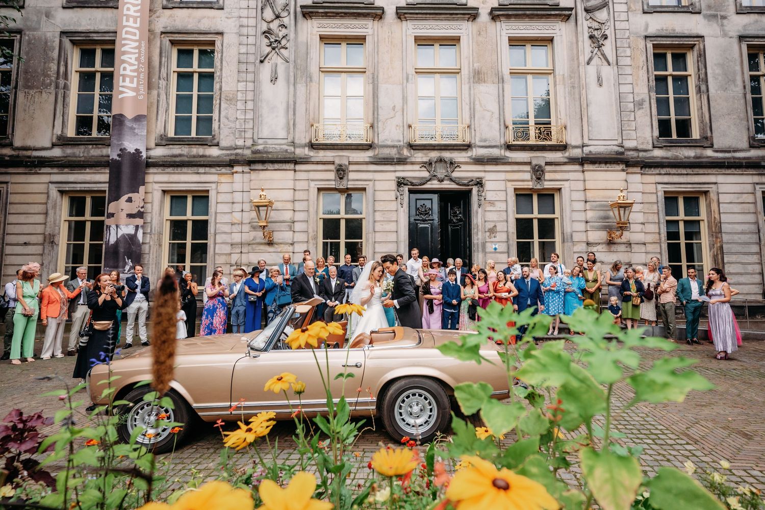 Receptie buiten met vintage auto en gele bloemen voor historisch stenen gebouw, bruidsfotografie Noordbrabants Museum Den Bosch, Brabant.
