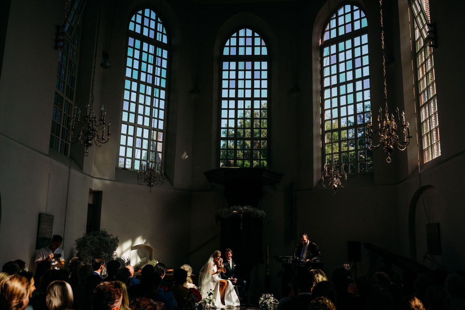 Interieur van historische kerk met bogen en dramatisch licht over trouwgasten, bruidsfotografie Brabant