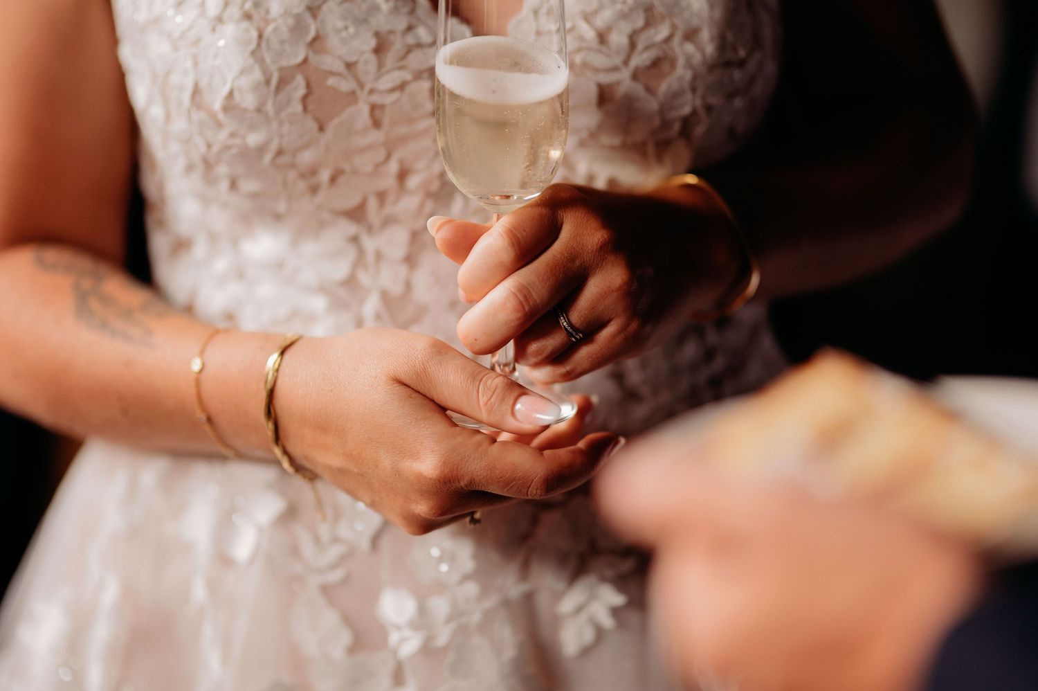 Close-up of bride holding champagne glass wearing gold bracelet and lace wedding dress during reception.
