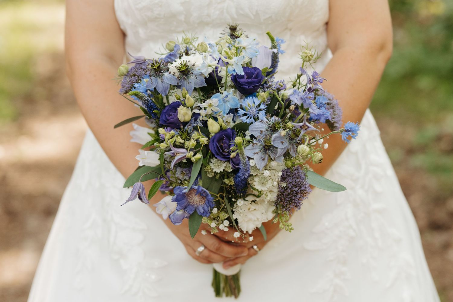 Bride holding a blue and white wedding bouquet with delphinium and wildflowers in a lace gown.