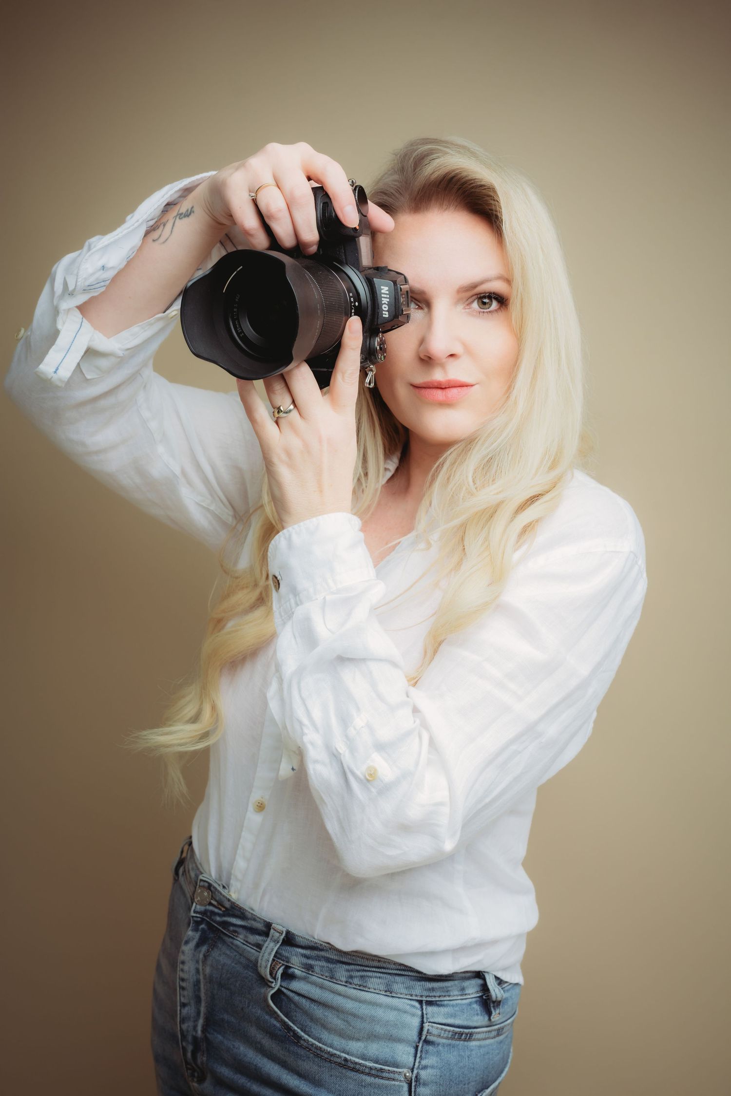 Fotograaf in wit overhemd en jeans poseert creatief tegen neutrale achtergrond, branding fotografie Brabant