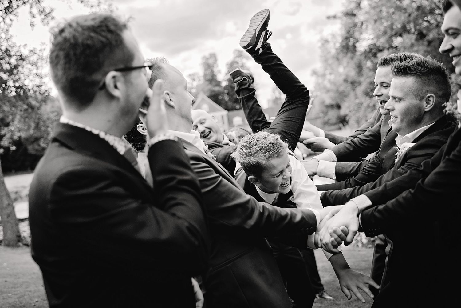 Zwart-wit foto van gasten die handen opsteken tijdens receptie, bruiloft Brabant.