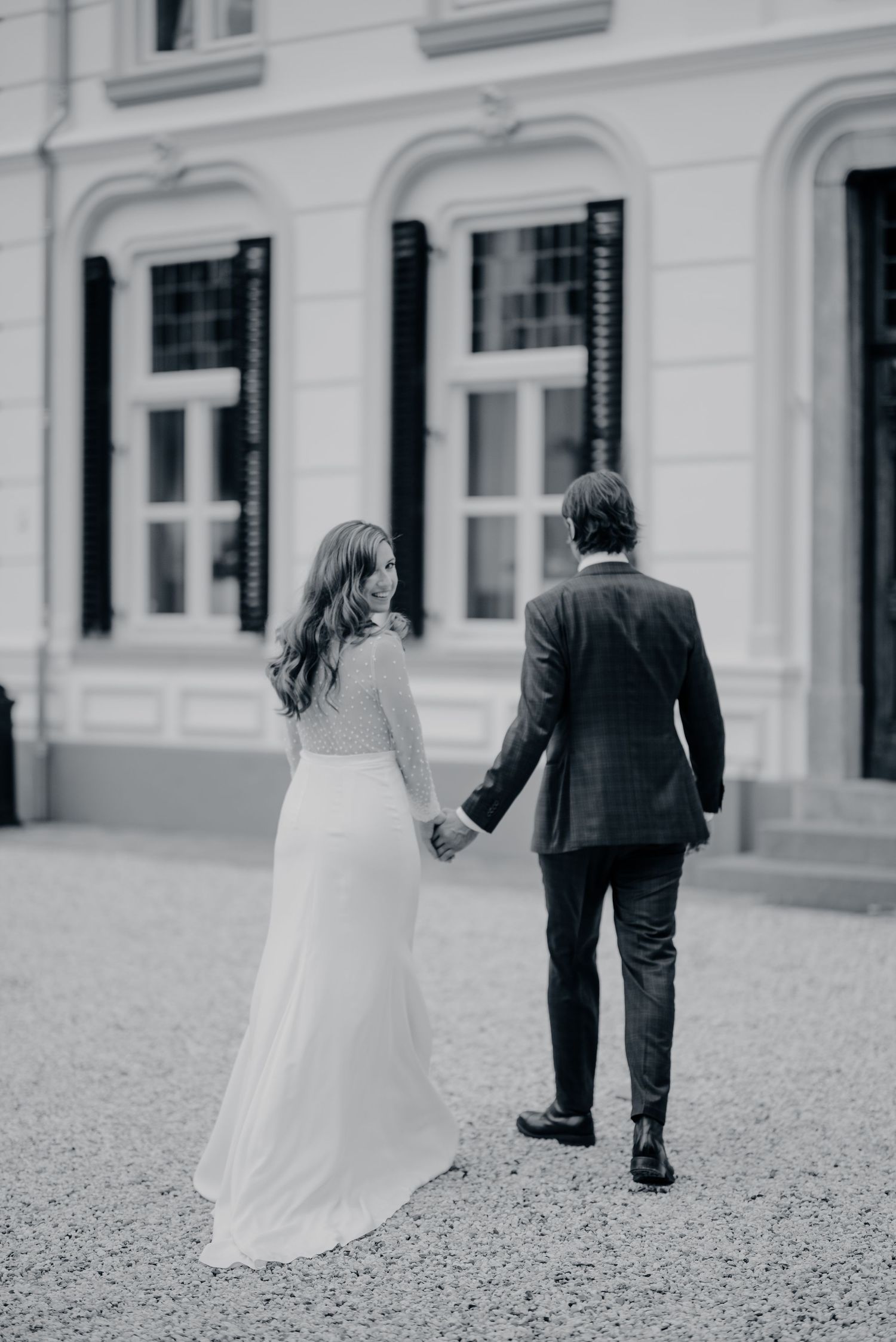 Zwart-wit serie van bruidspaar dat samen over grindpad loopt in elegante trouwkleding, bruidsfotografie Noordbrabants Museum Den Bosch, Brab