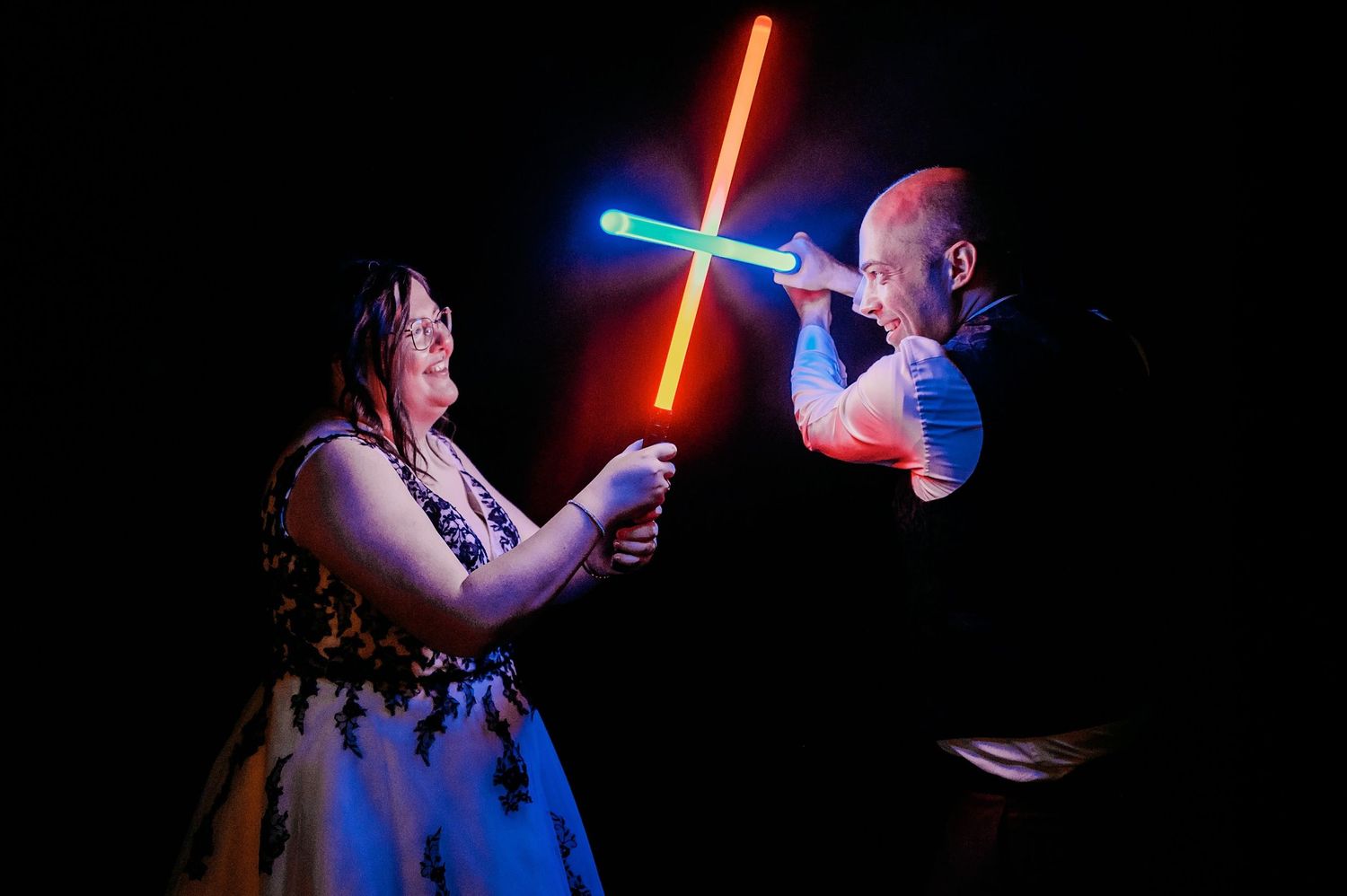 Glowing lightsabers illuminate a dark room during a wedding reception party.
