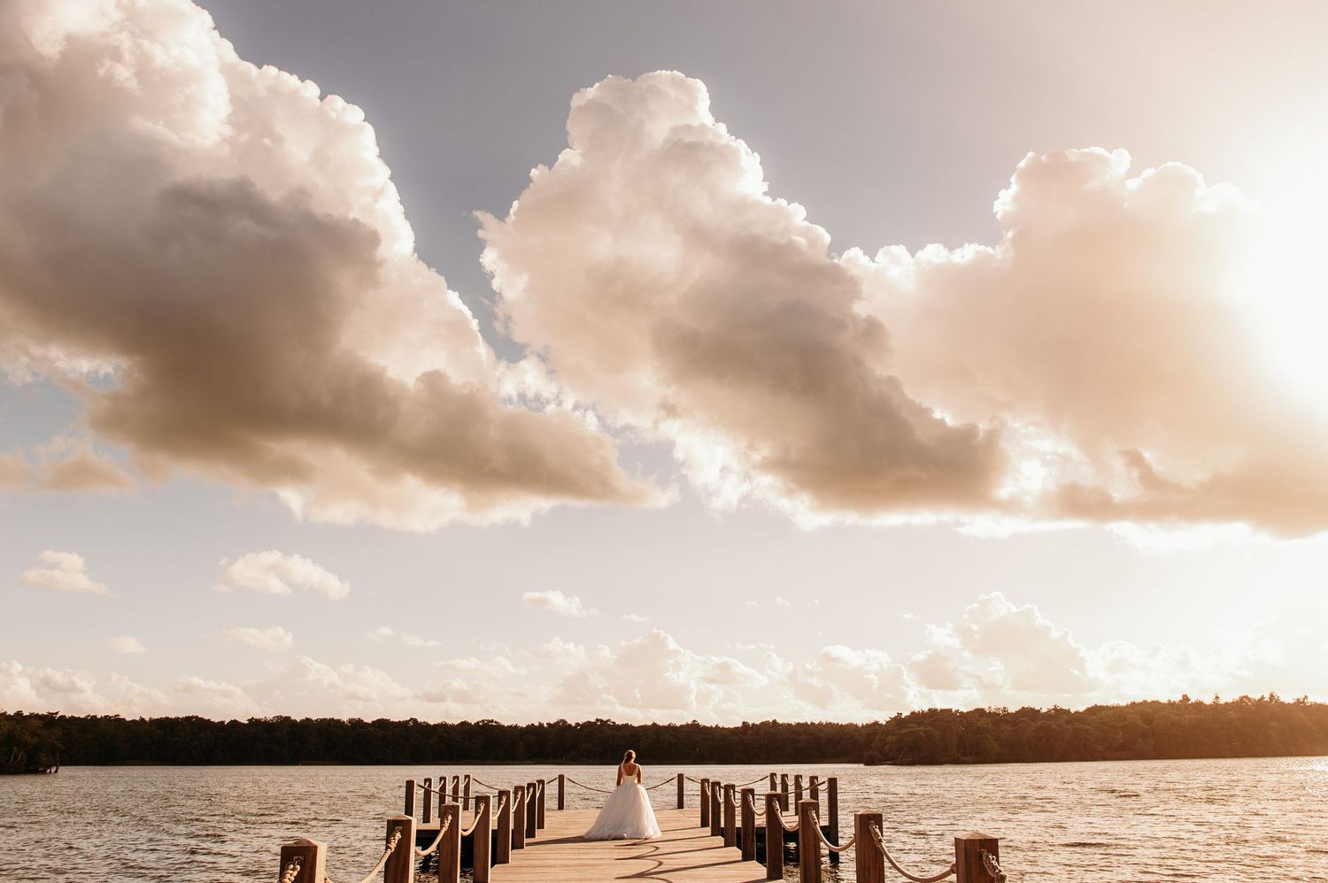 Dramatische zonsondergangsilhouetten op houten pier over kalm water met bewolkte lucht, bruidsfotografie Brabant