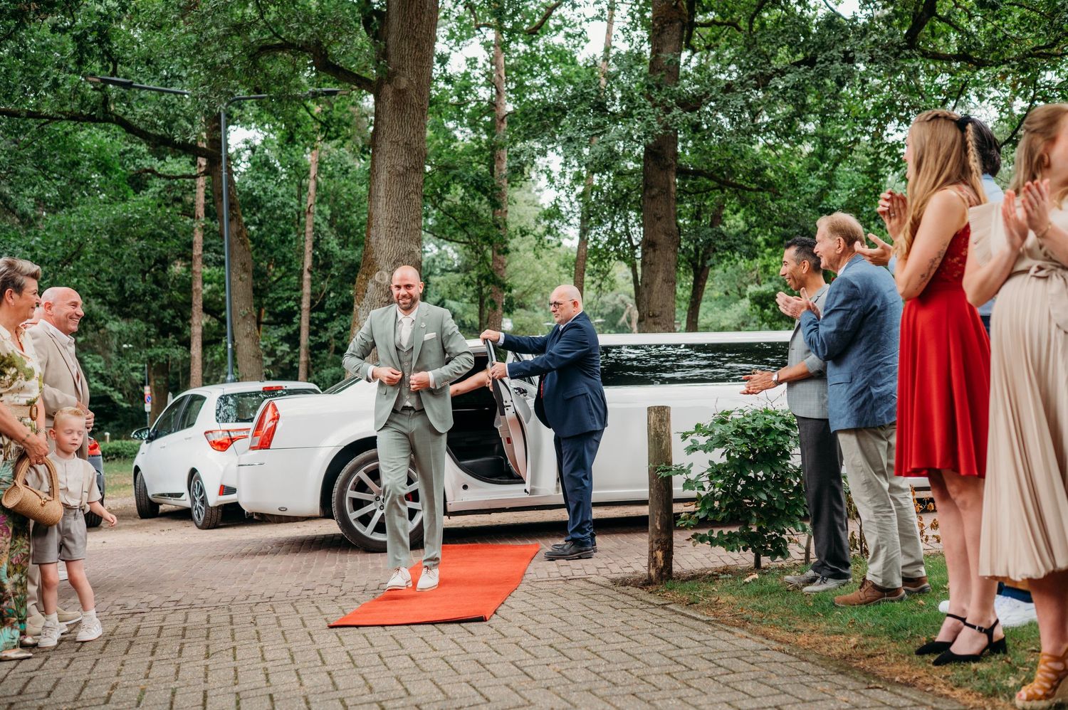 Gasten verzamelen op bakstenen pad bij auto voor buitenceremonie, bruidsfotografie IJM IJzereman Vught, Brabant.