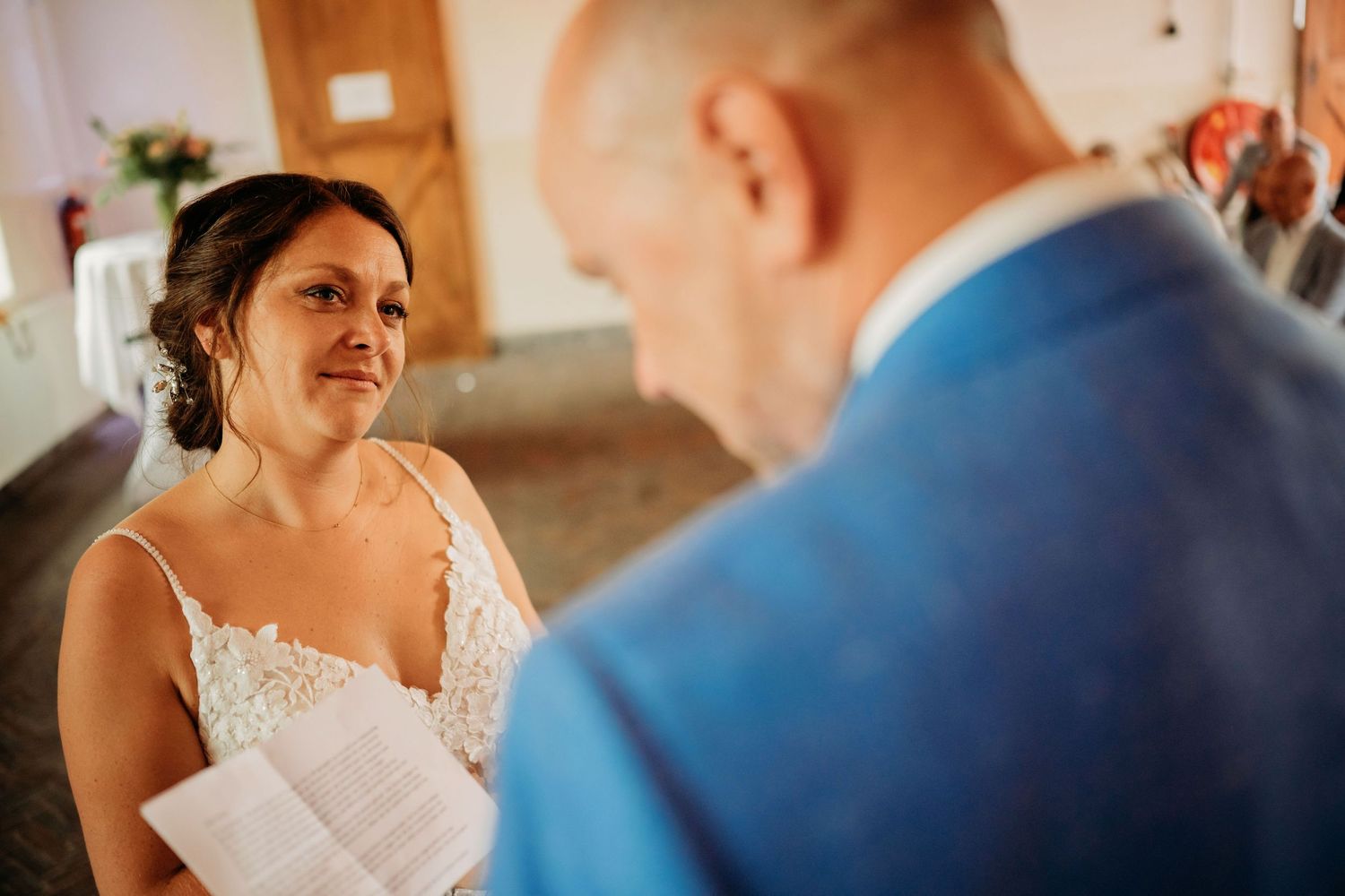 Emotional bride in lace gown exchanges heartfelt vows with groom in blue suit at ceremony.