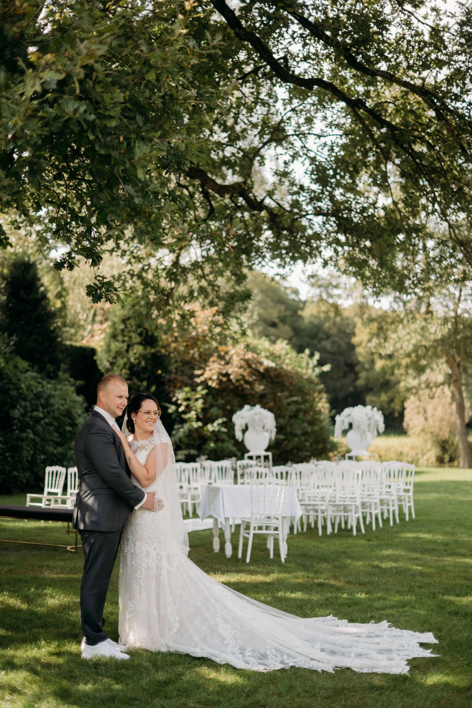 Outdoor trouwceremonie met witte stoelen onder boomkroon, bruidsfotografie Brabant