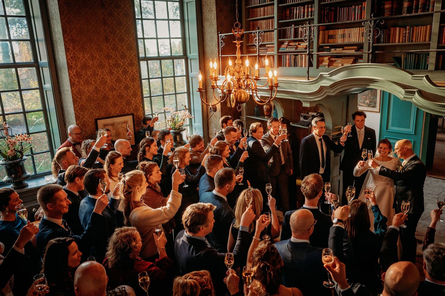Grote groep bruiloftsgasten in sfeervolle zaal met warm licht, spontane bruidsfotografie bij Kasteel Wijenburg Echteld, Brabant.