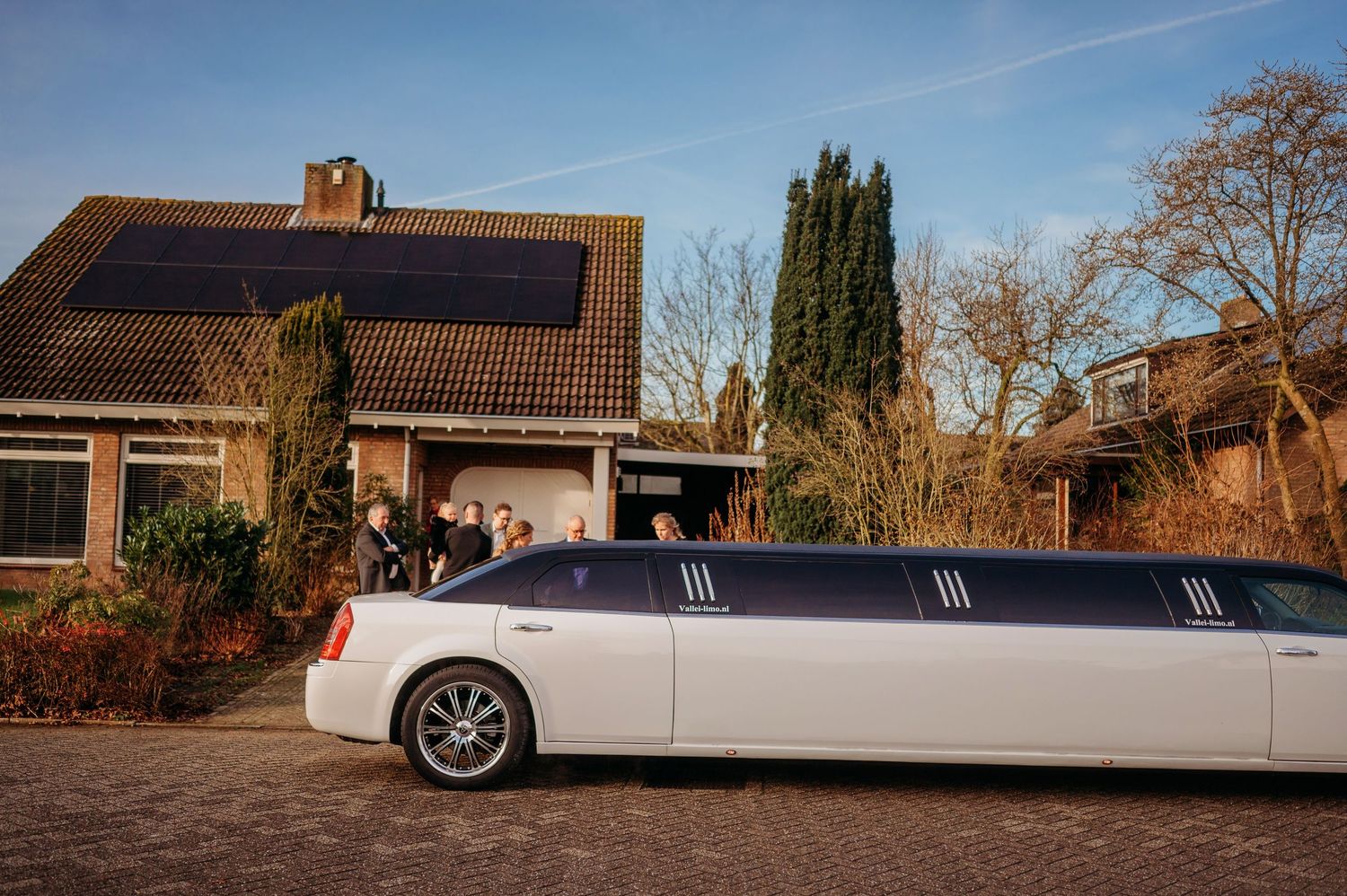 Witte limousine geparkeerd voor huis met zonnepanelen, sfeervolle bruidsfotografie bij Boscafé Oisterwijk, Brabant.