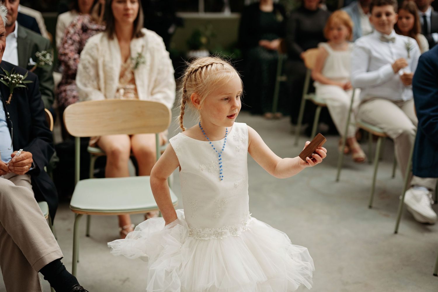 Young flower girl in white tutu dress walks down the wedding ceremony aisle.
