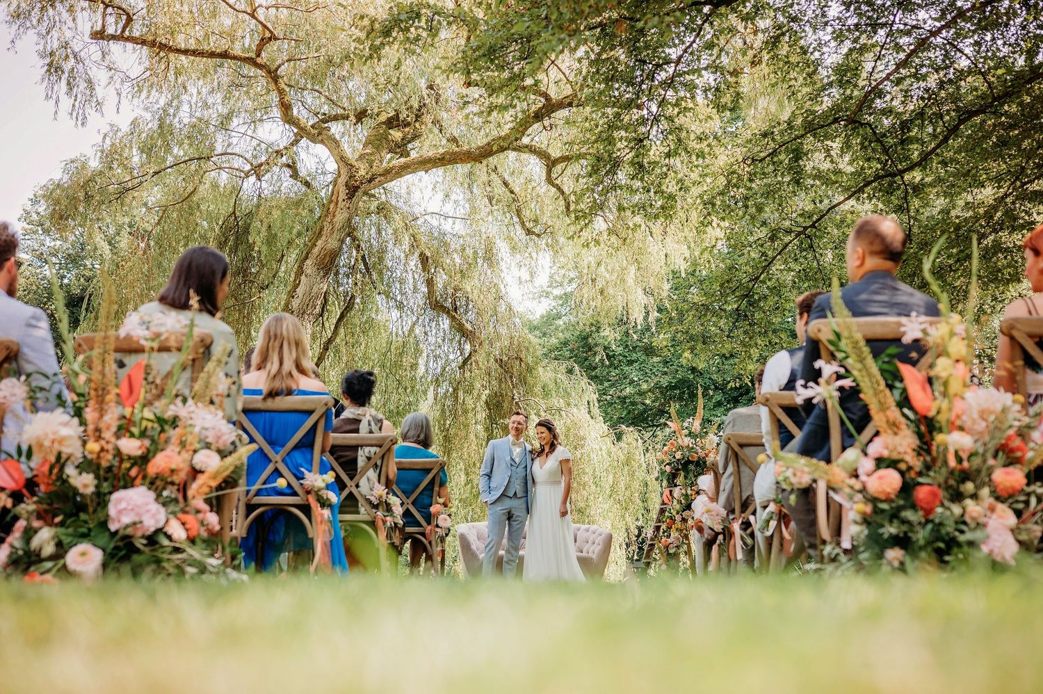 Panoramisch overzicht van buitereceptie met bloemen en wilgenbomen, bruidsfotografie Brabant