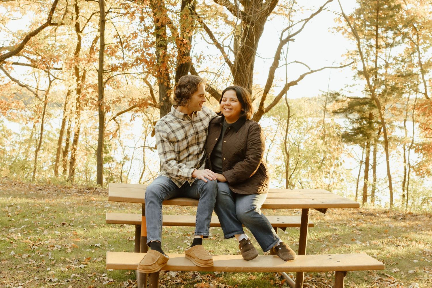 Couple sitting together on a wooden bench in an autumn park surrounded by colorful fall foliage.