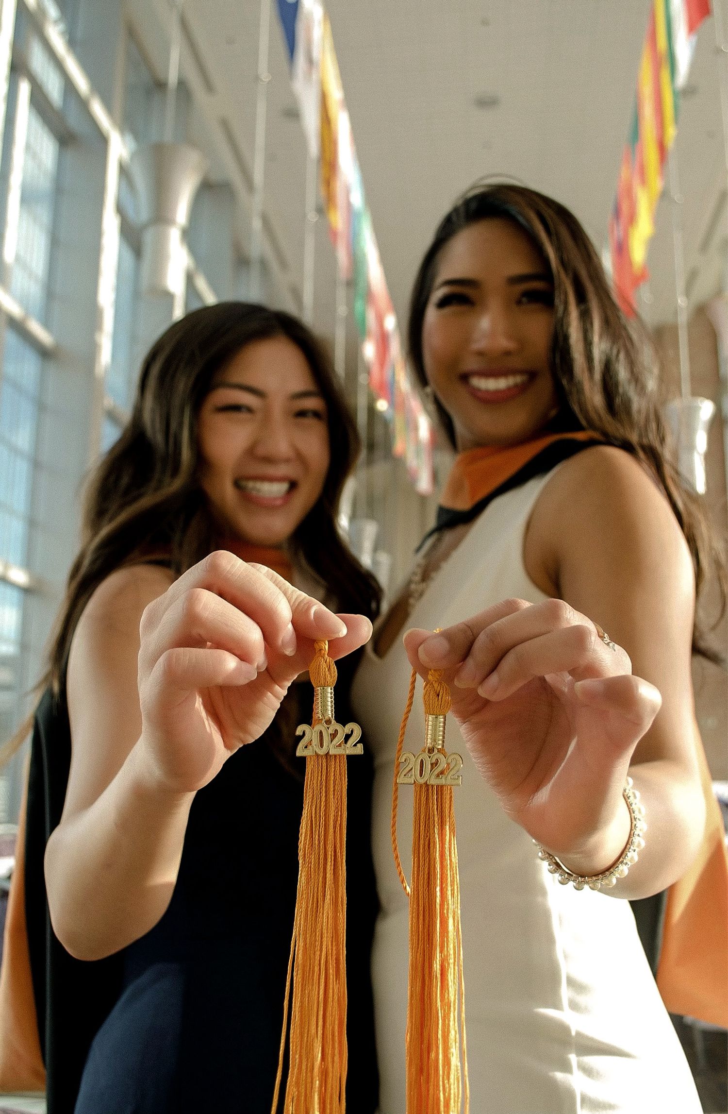 Two graduates showing off their 2022 graduation tassels in a hallway with colorful flags.