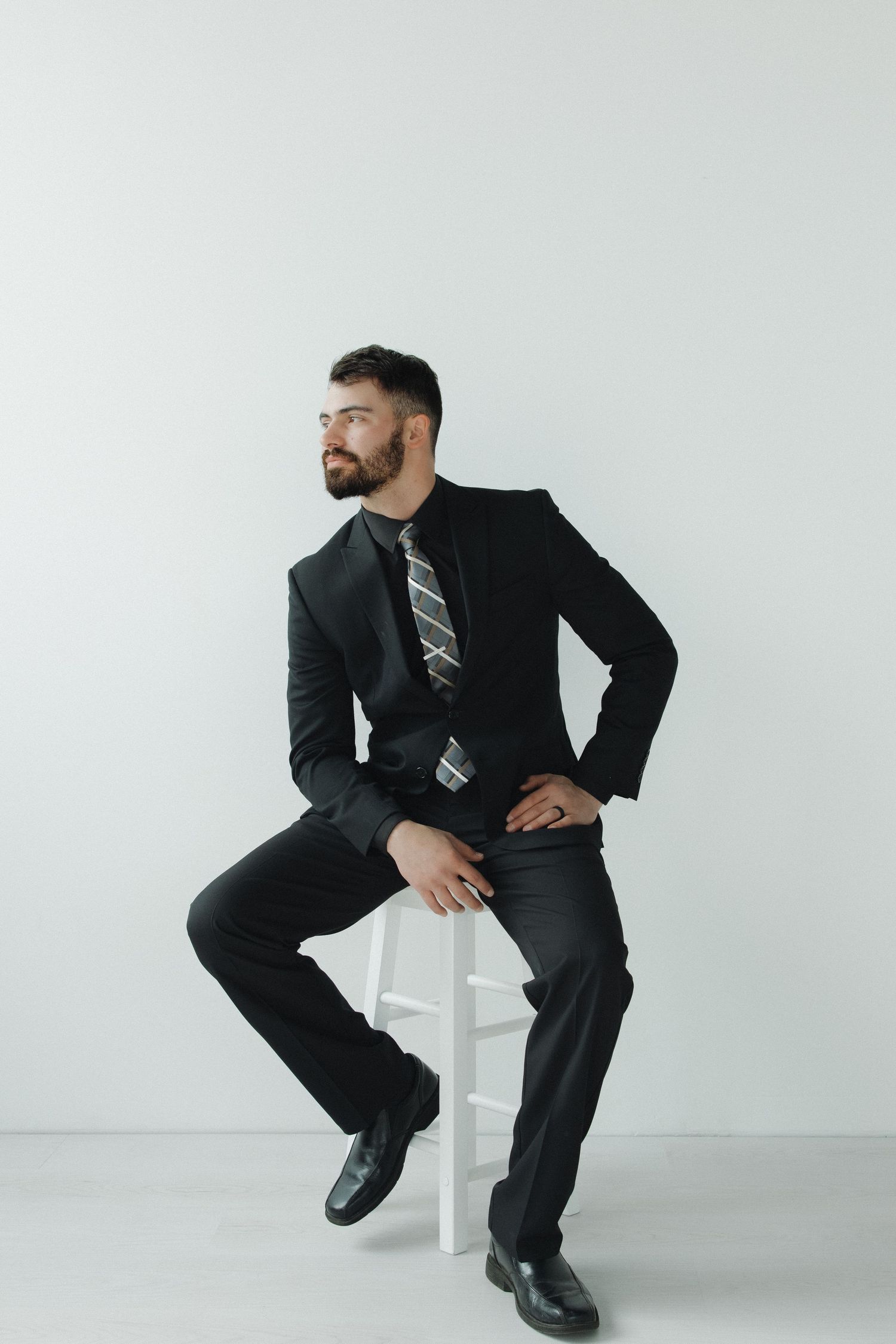 Four minimalist studio shots of a person in a dark business suit sitting on a white stool against a white background.