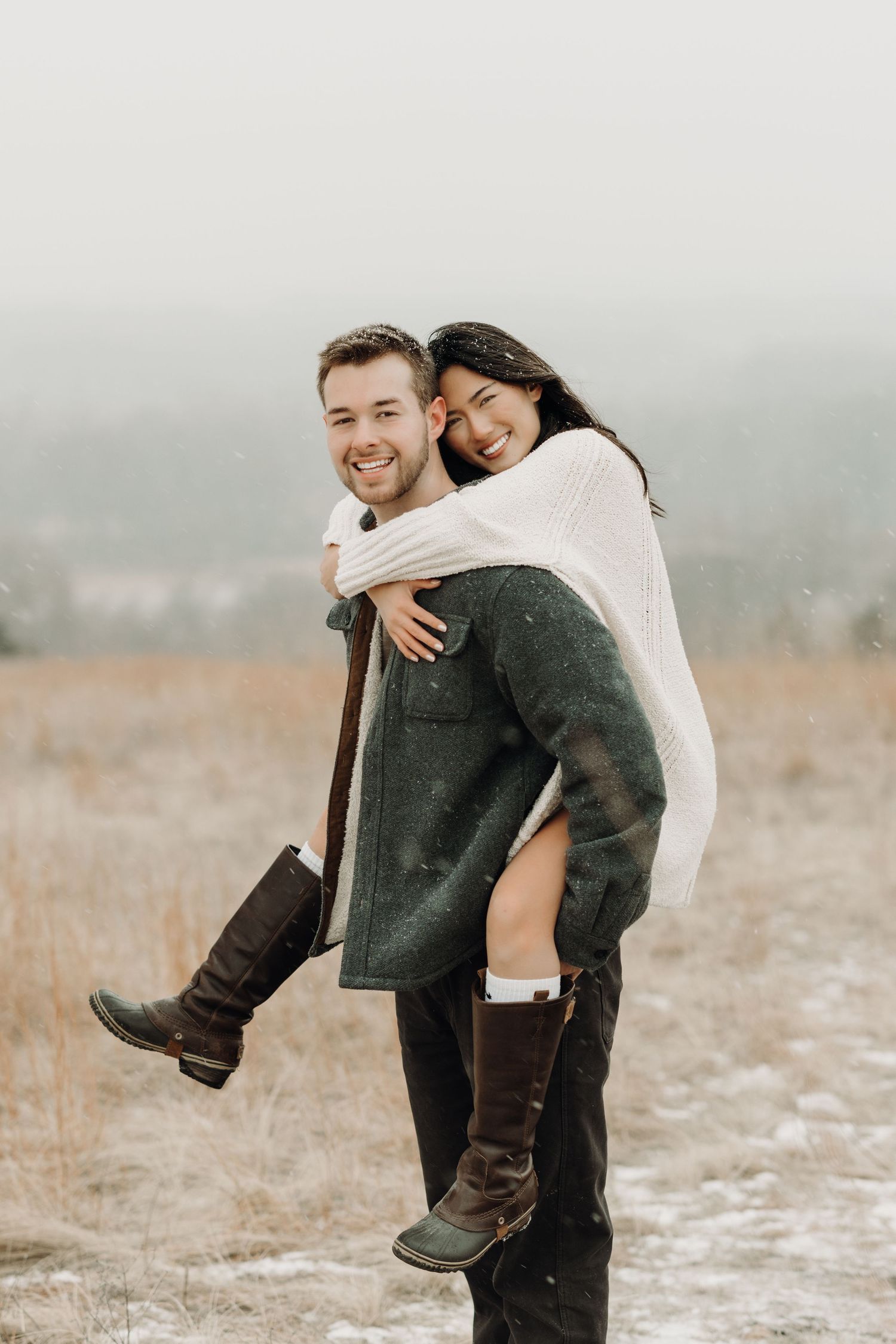 A couple shares playful and romantic moments in a misty winter field while wearing cozy sweaters.