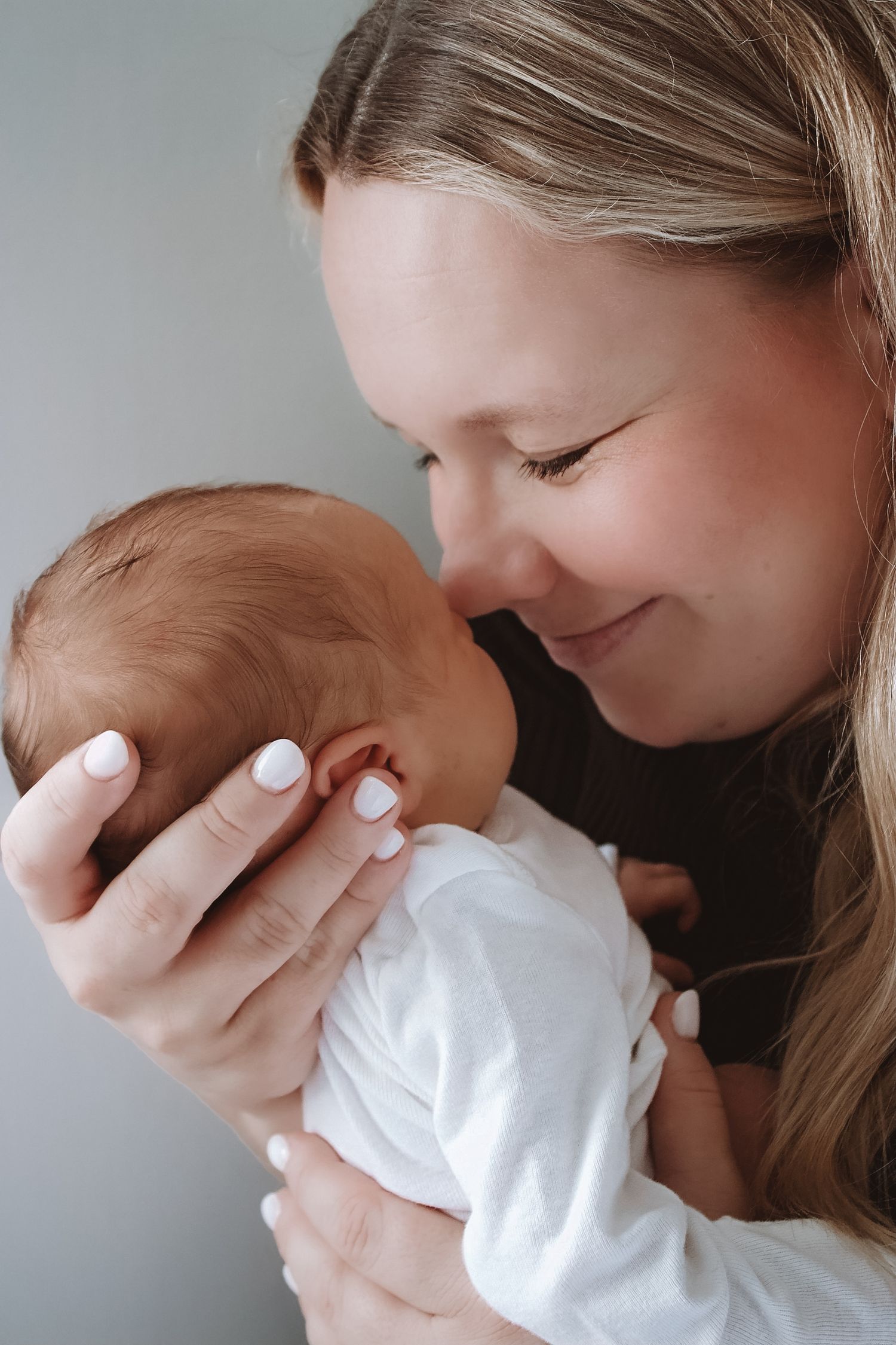 A smiling mother tenderly holds her newborn baby close, nuzzling the infant dressed in white.