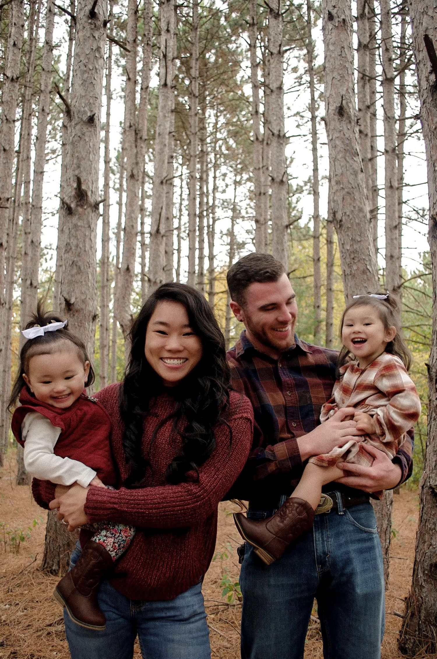 Family having fun together in pine forest wearing coordinated red and burgundy outfits.