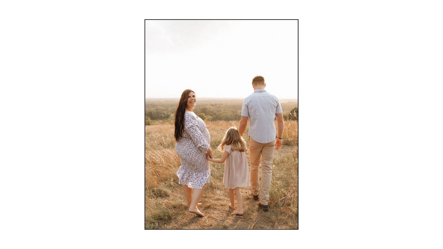 Couple holding hands while standing in a golden field at sunset wearing white and neutral colored clothing.