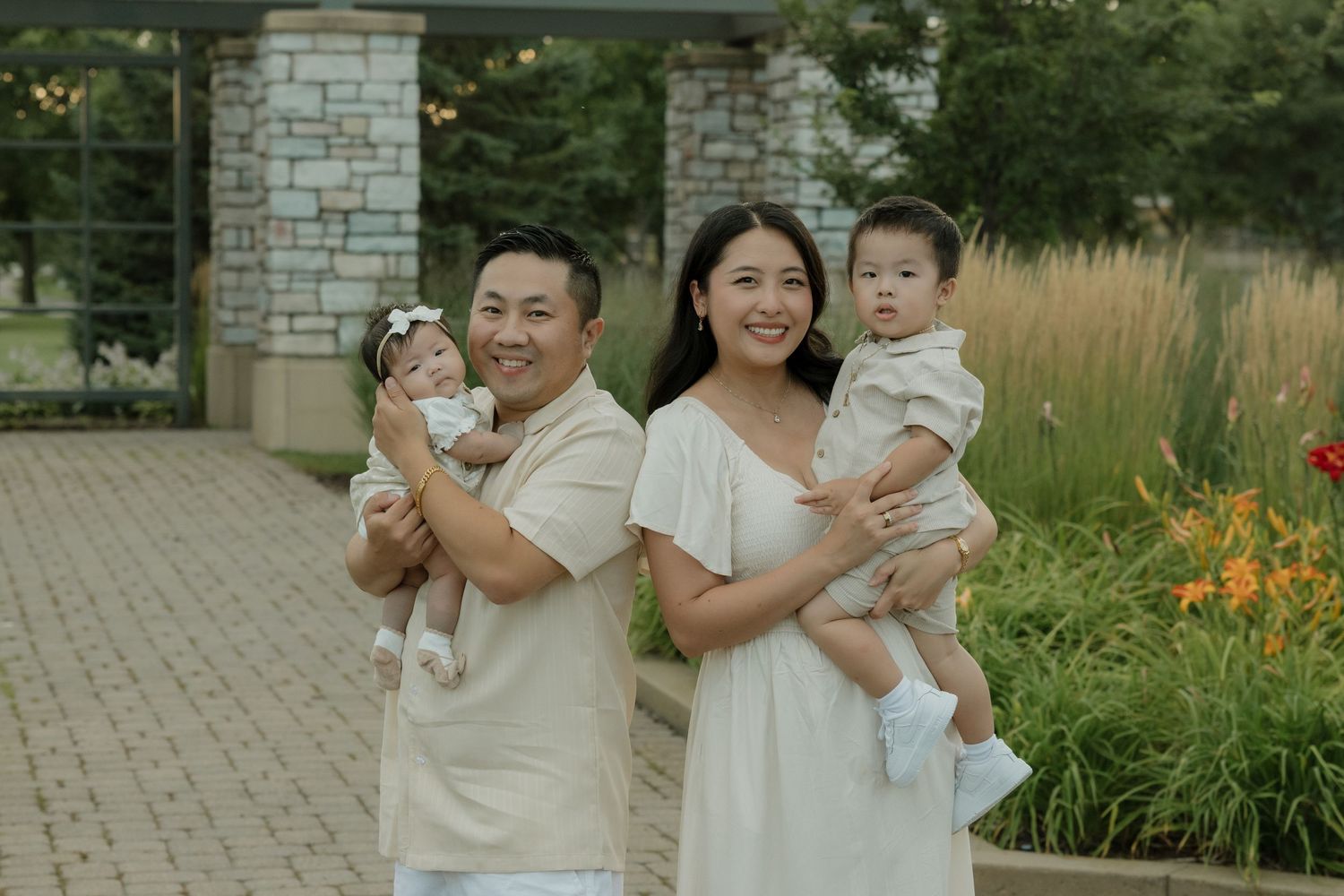 A group wearing cream-colored outfits poses together in a garden setting with stone walls and orange flowers.