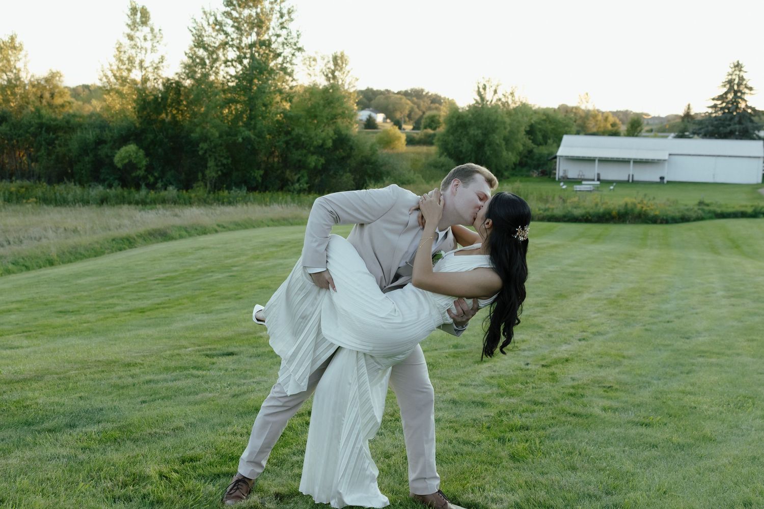 Two people in white outfits perform a graceful dance move together on a grassy lawn at sunset.