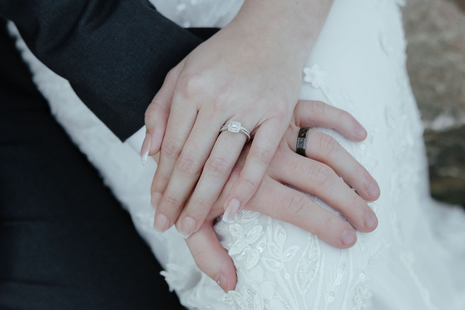 Close-up details of intricate lace and beading on a white wedding dress with hands delicately touching the fabric.