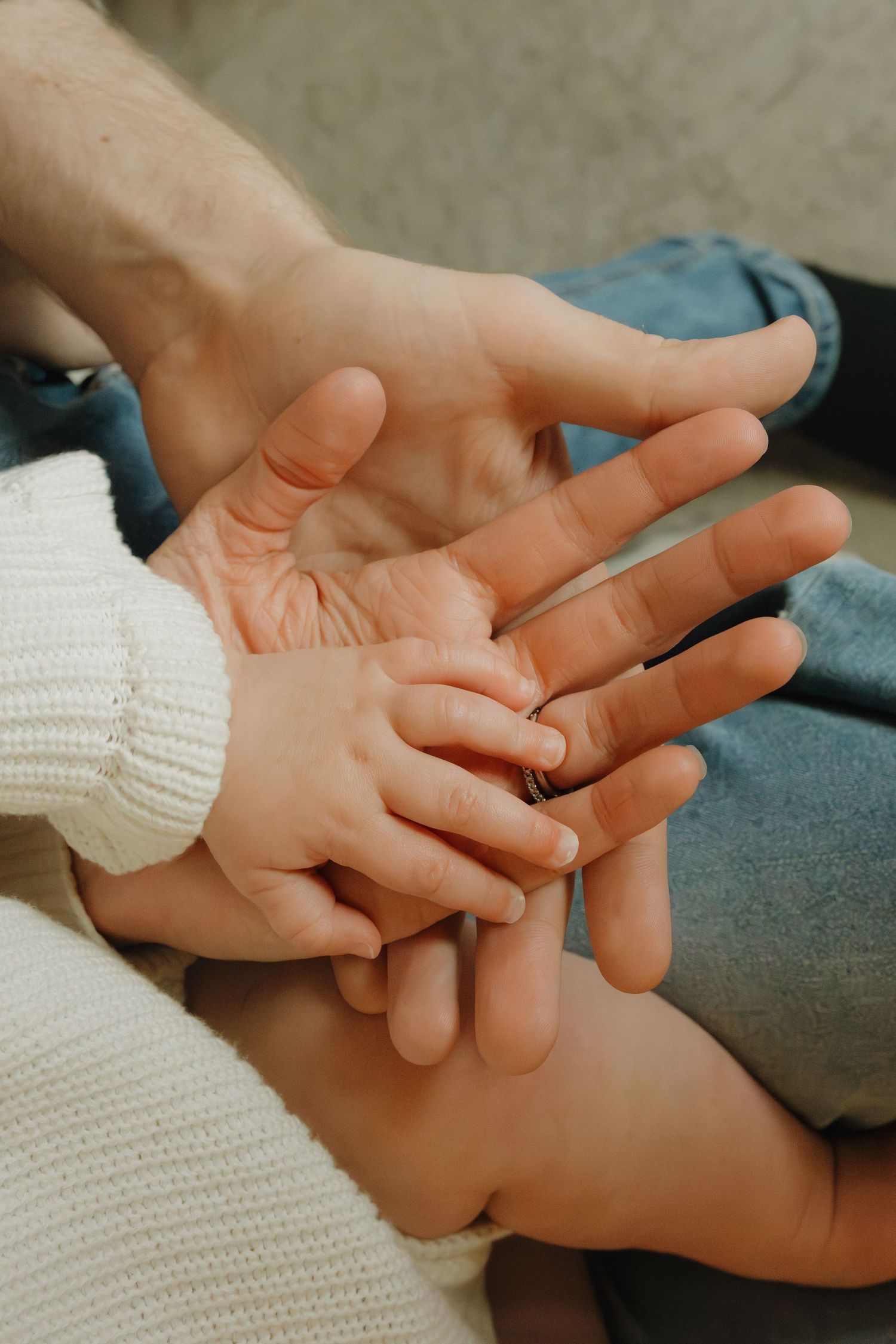 A baby's tiny hand resting on top of two adult hands, symbolizing family love and connection.