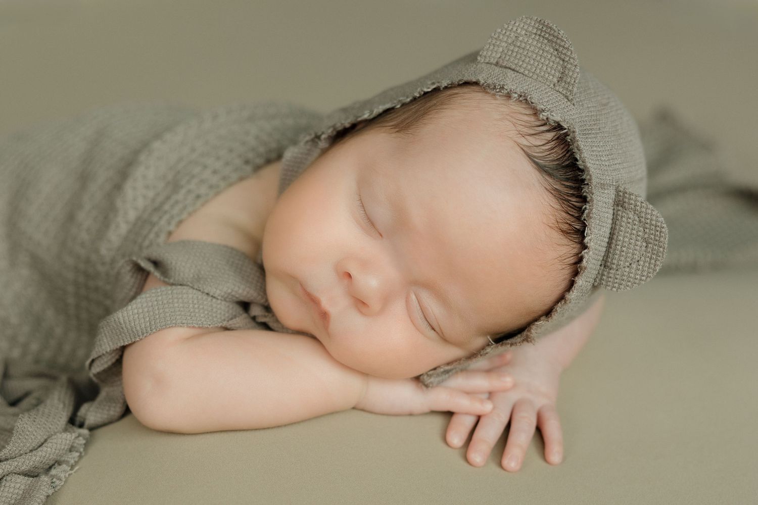 Sleeping newborn baby in soft sage green wrap photographed from multiple angles during professional photoshoot.