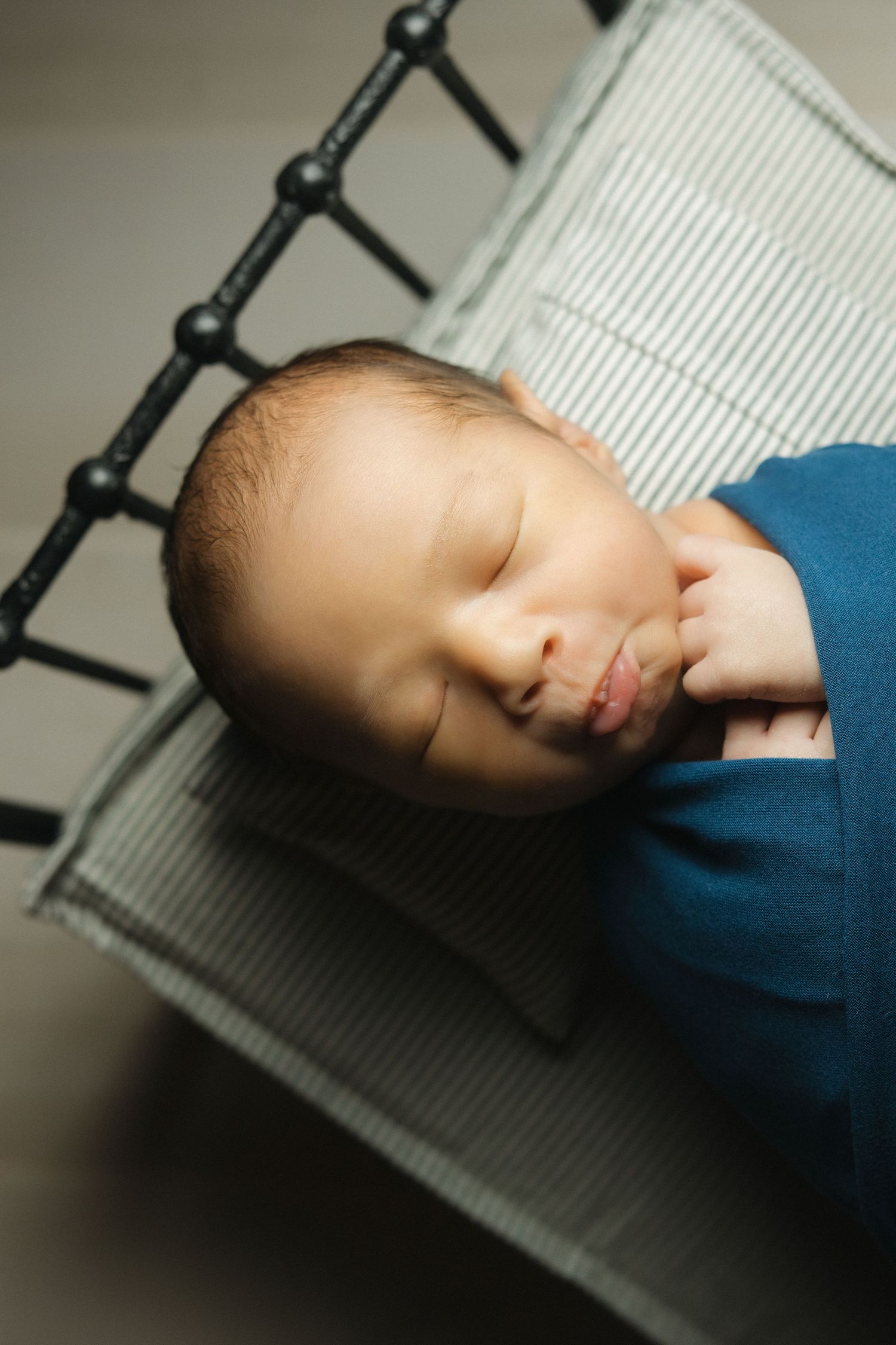 A sleeping baby in a blue outfit rests peacefully against a white and black striped surface.