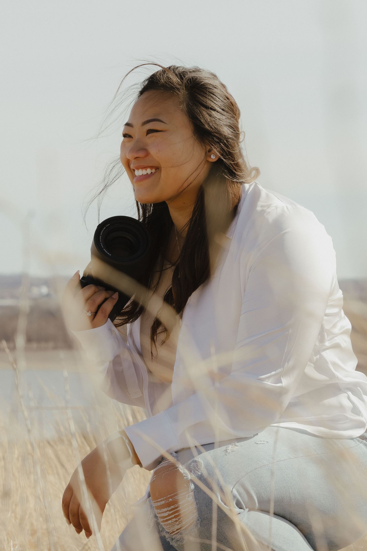 Joyful expression captured in a candid moment wearing white jacket in golden field with windswept hair.