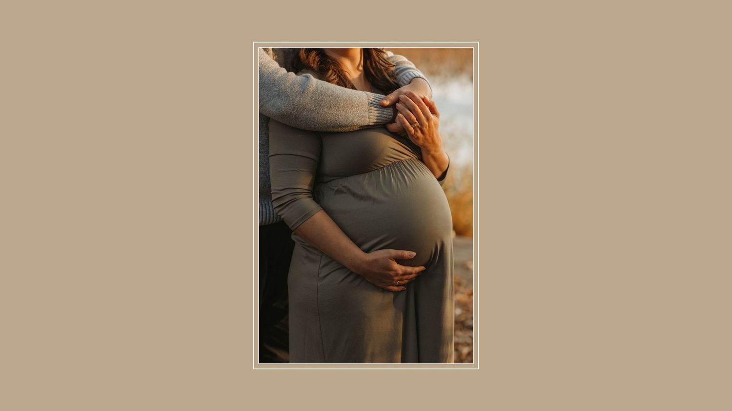 Close up photograph of hands cradling a pregnant belly in soft window light.