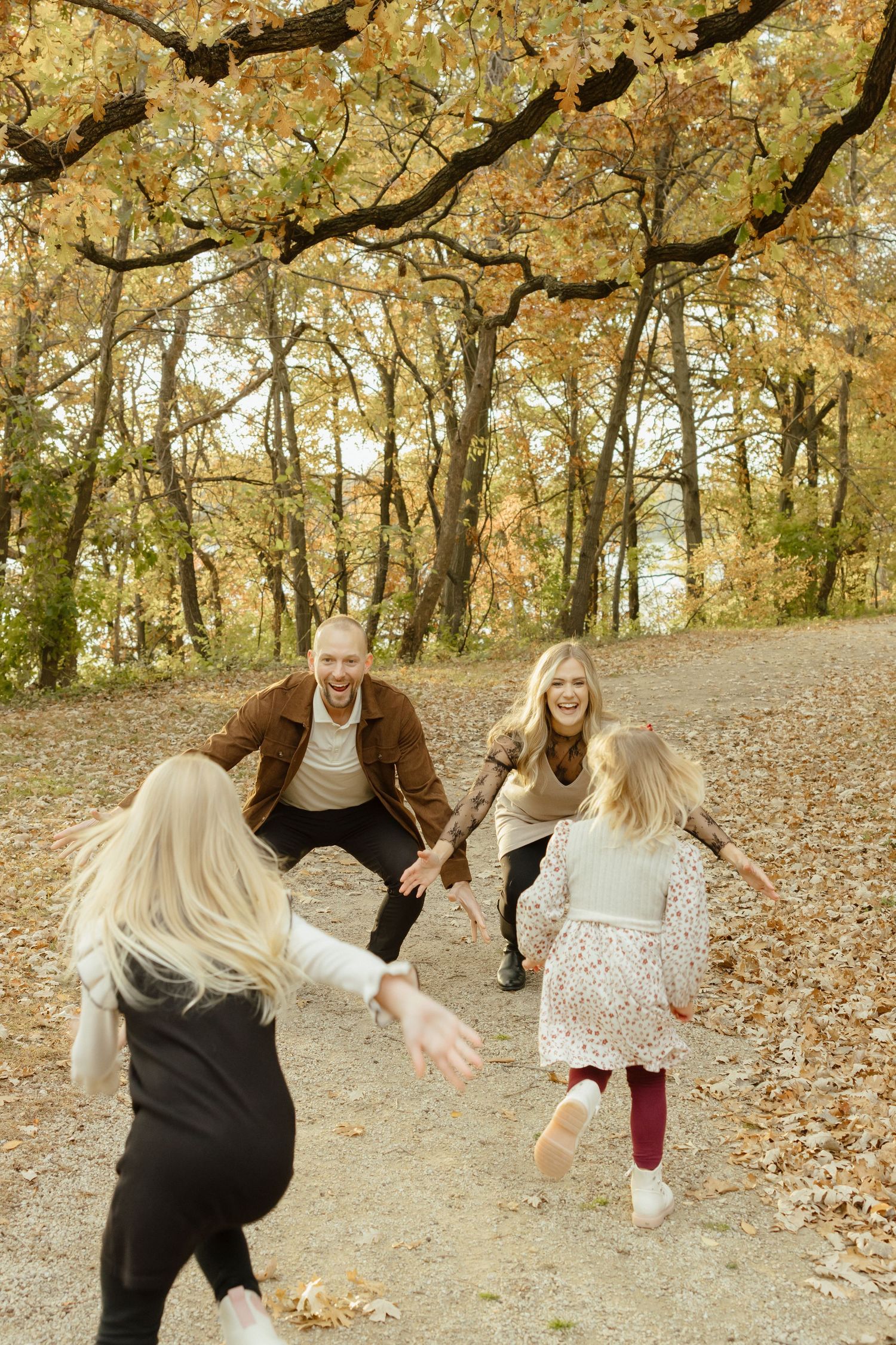 Family running toward each other with open arms in an autumn forest, laughing and playing among golden fallen leaves.