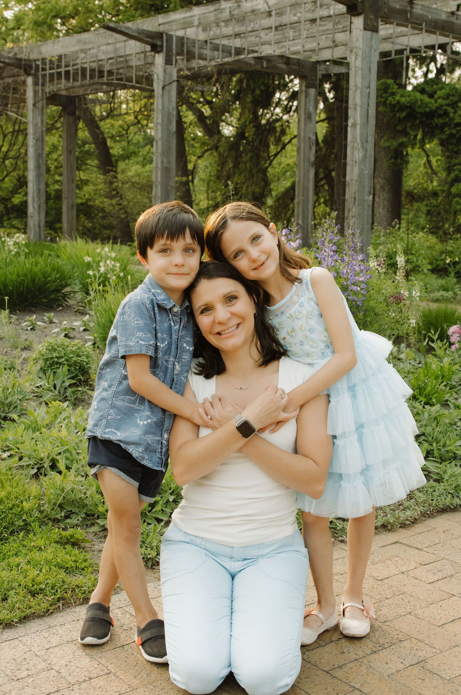 Family portrait in garden setting with pergola and purple flowers.