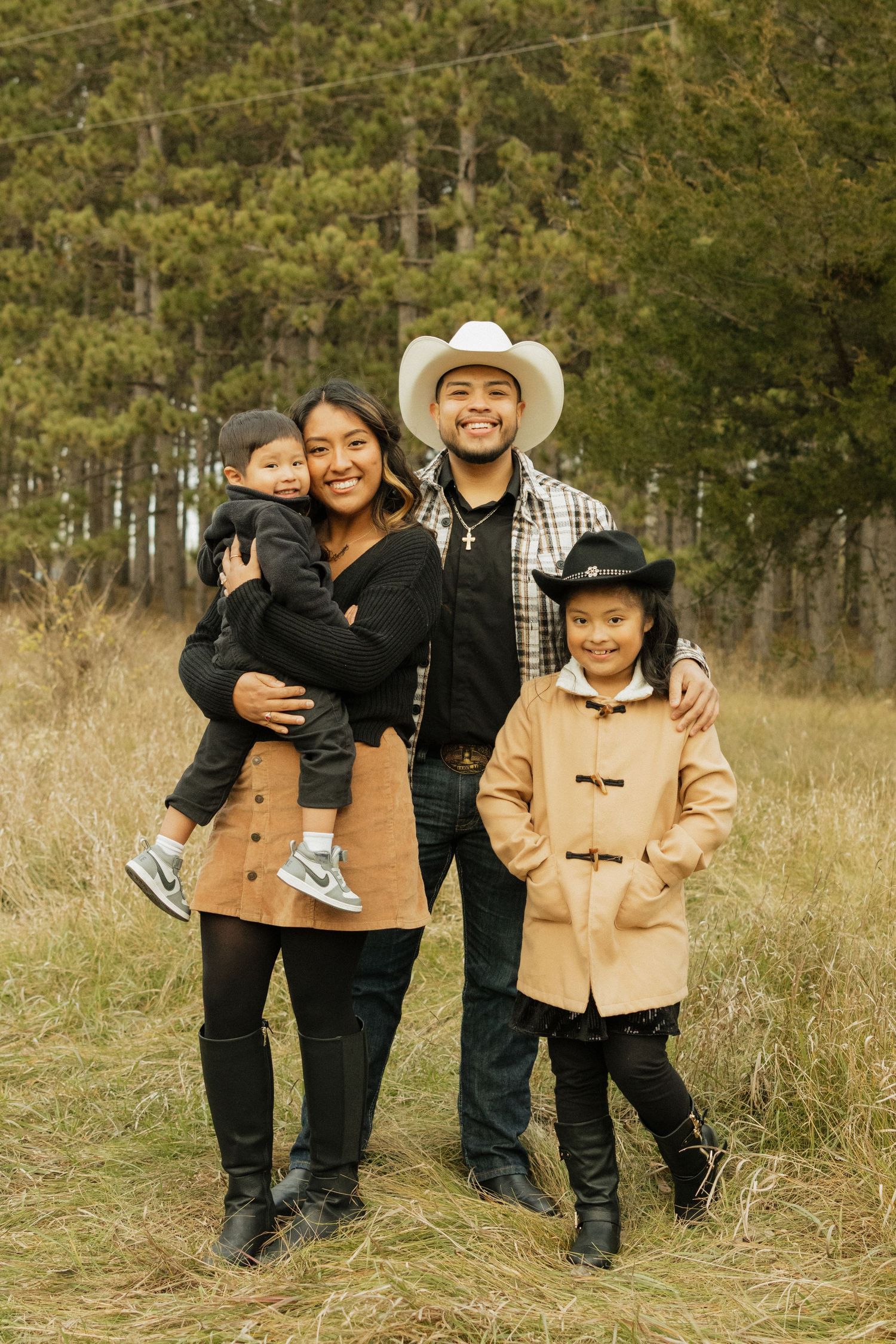 Family wearing matching western outfits posing together in a grassy field with trees in the background.