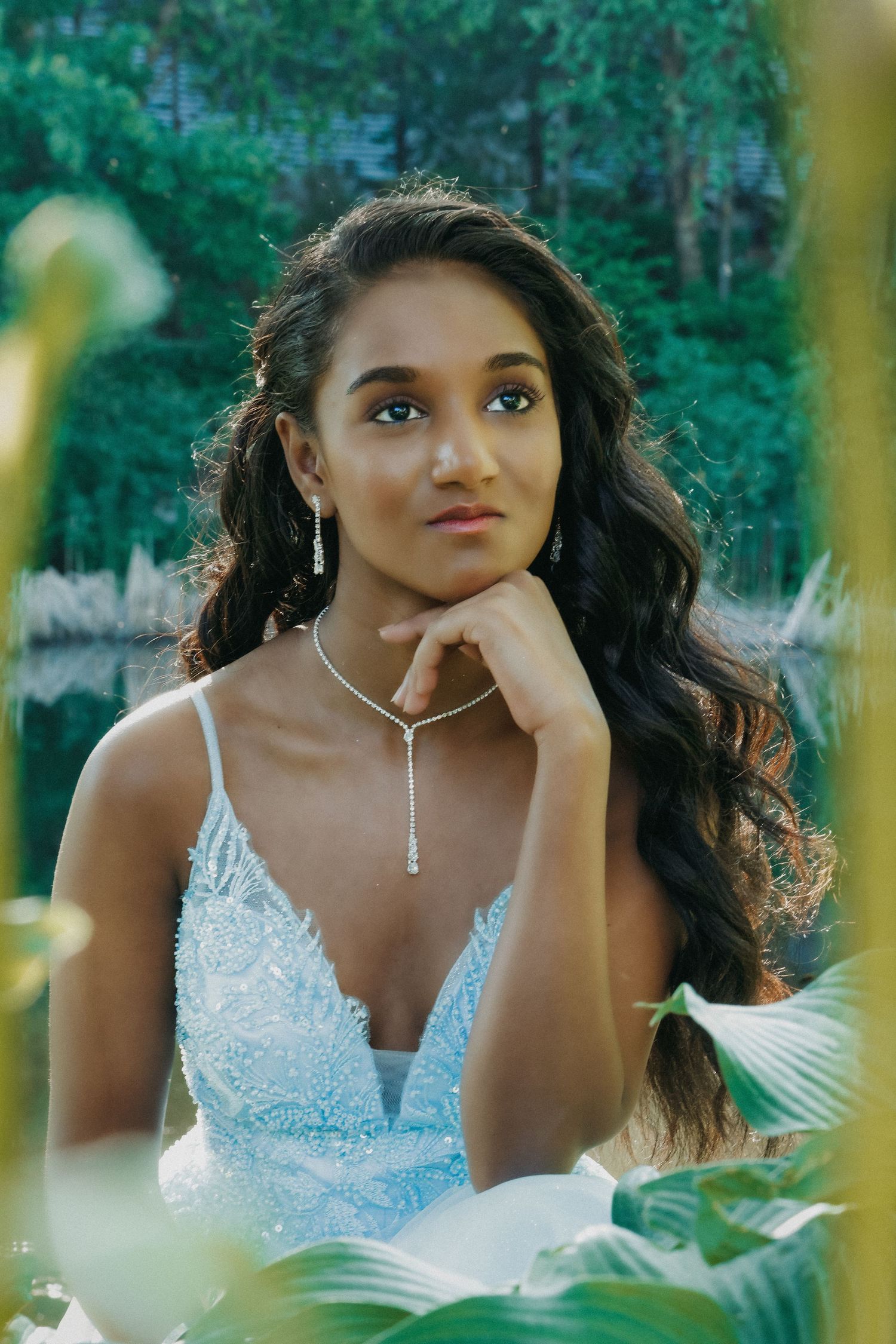 A bride in a white lace dress poses thoughtfully in a garden setting.