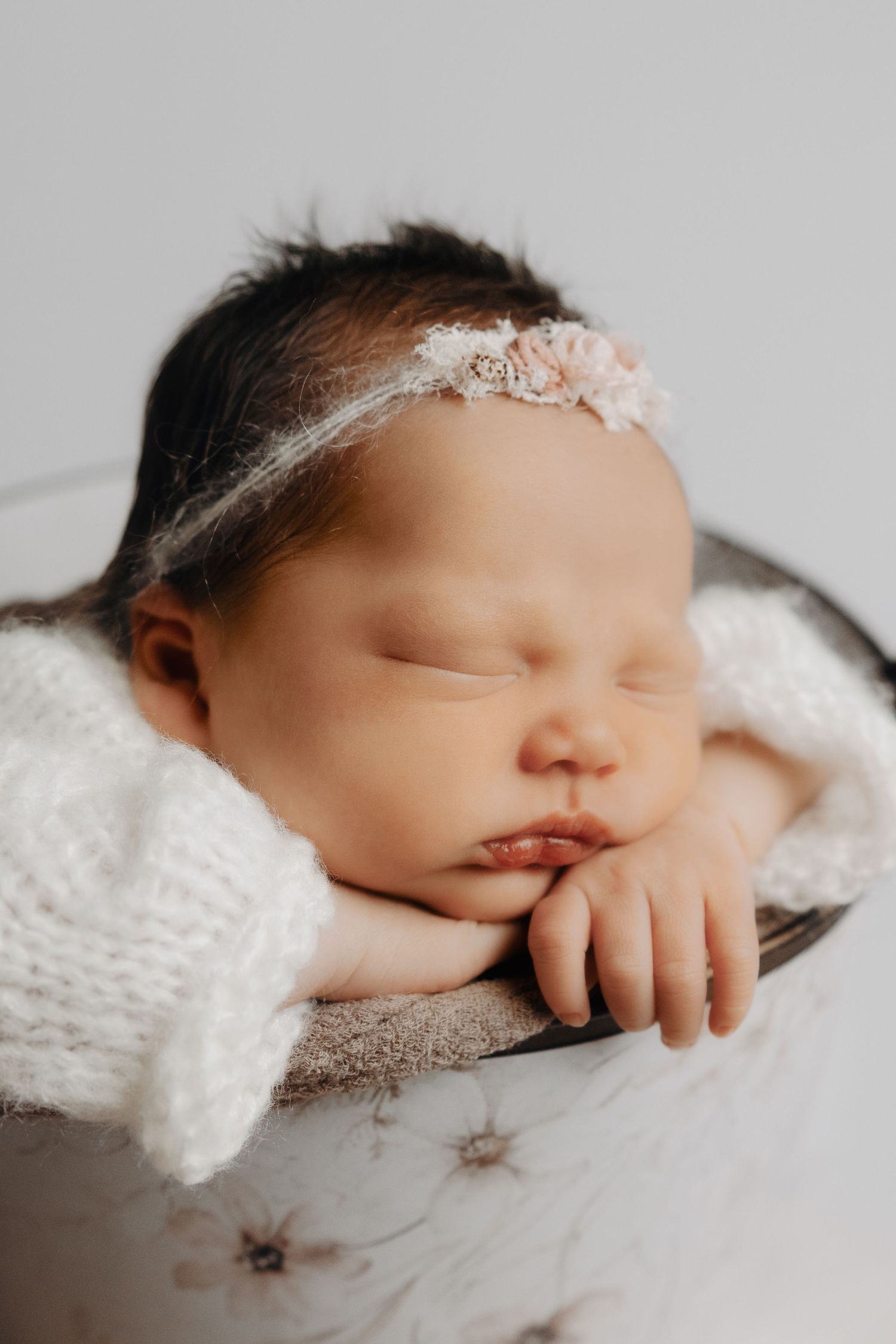 Sleeping newborn baby girl wearing a delicate floral headband, resting peacefully in a decorative bowl.