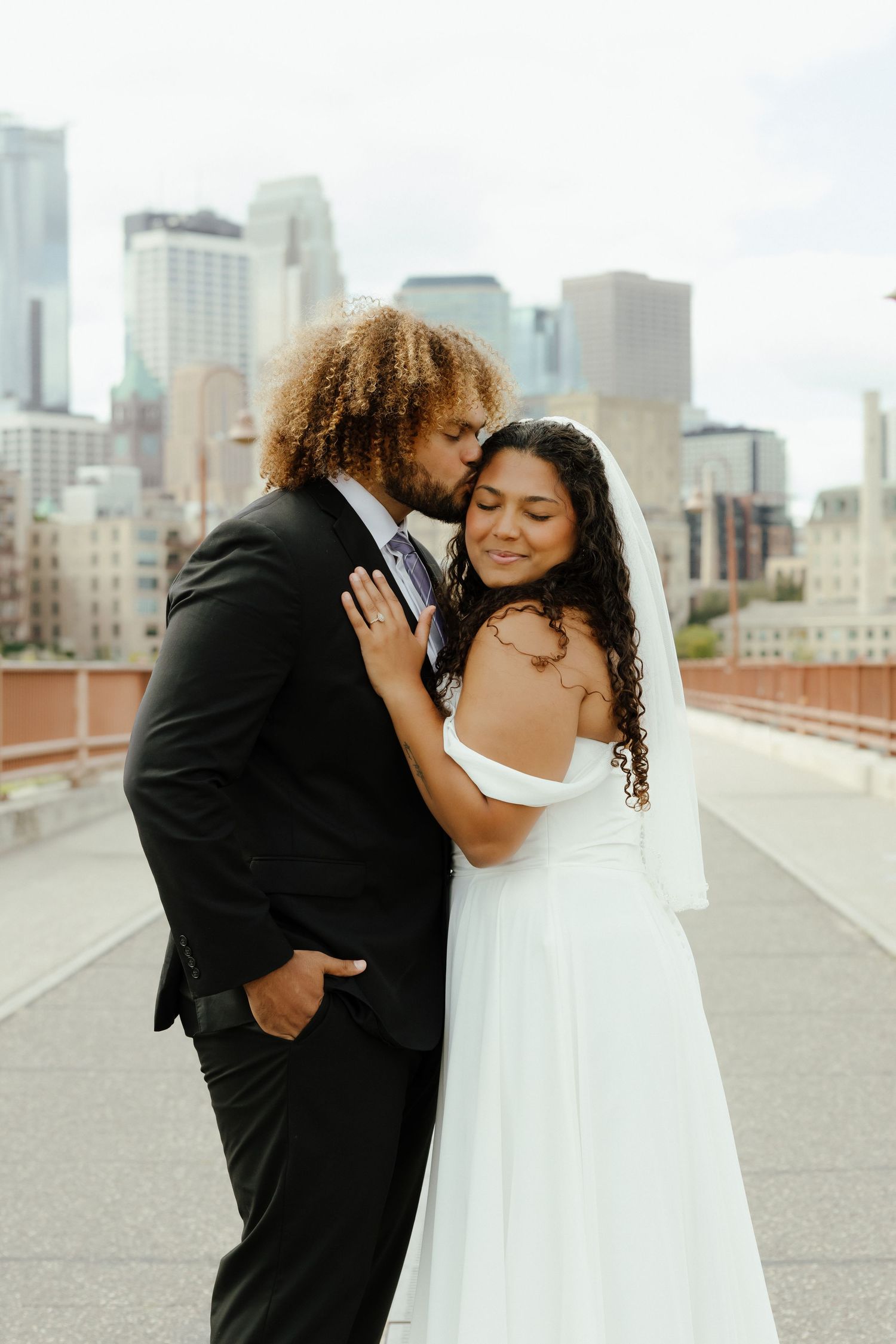 A couple in wedding attire share intimate moments on a rooftop with a city skyline in the background.