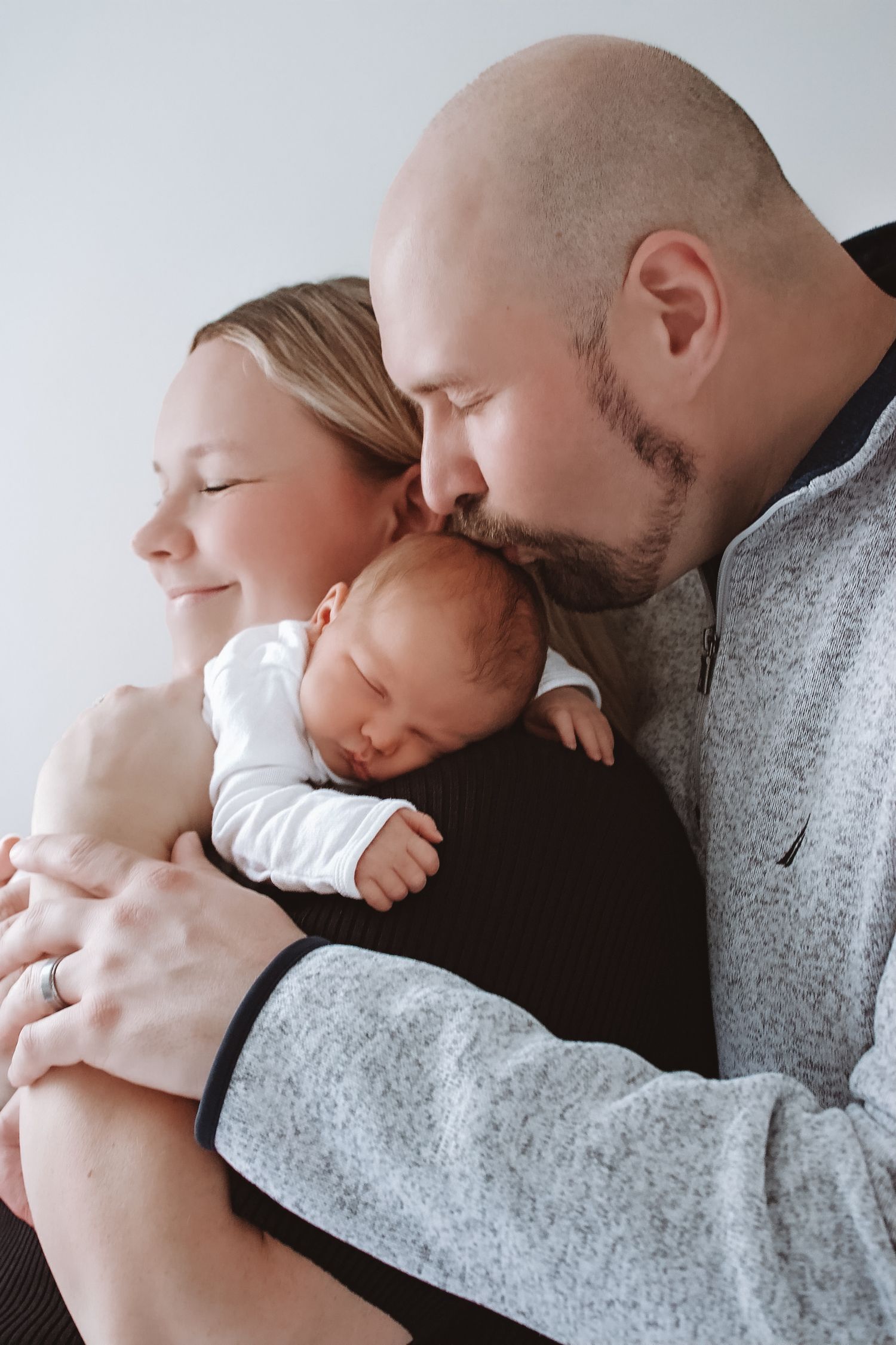 New parents tenderly kissing their sleeping newborn baby together in a heartwarming family portrait.