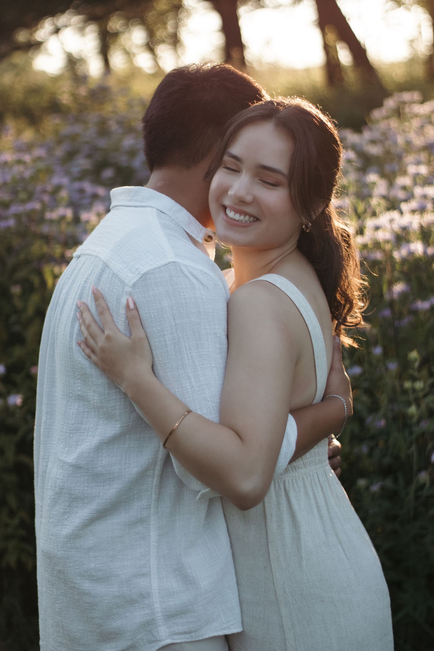Couple embracing in sunset garden with white flowers blooming in background.