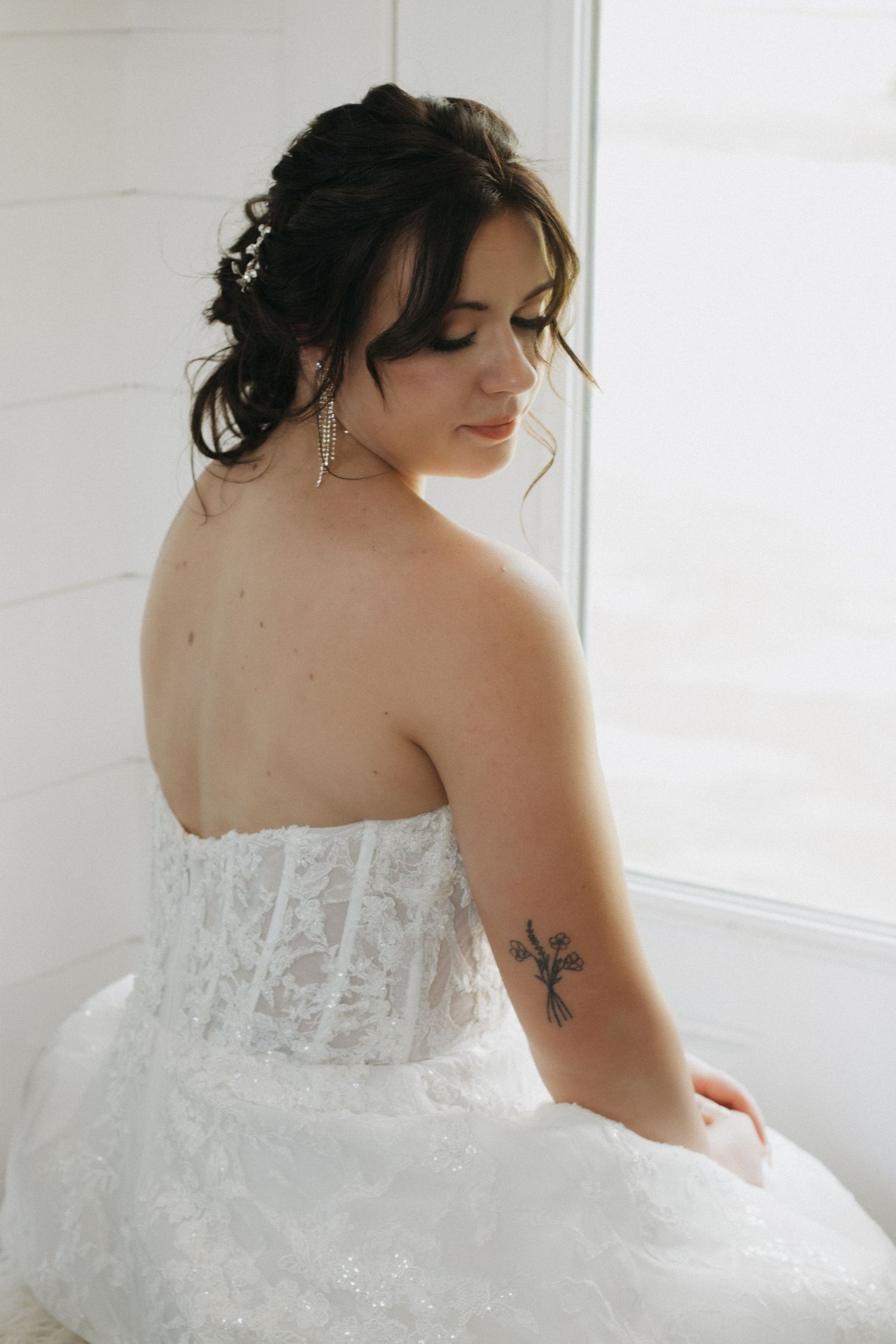 Back view of bride in white lace strapless wedding dress with delicate tattoo detail on shoulder.