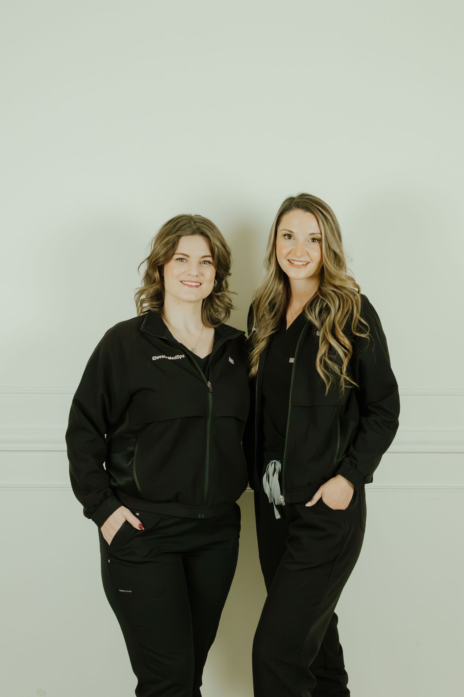 Two people wearing matching black scrubs or medical uniforms pose together against a light colored wall.