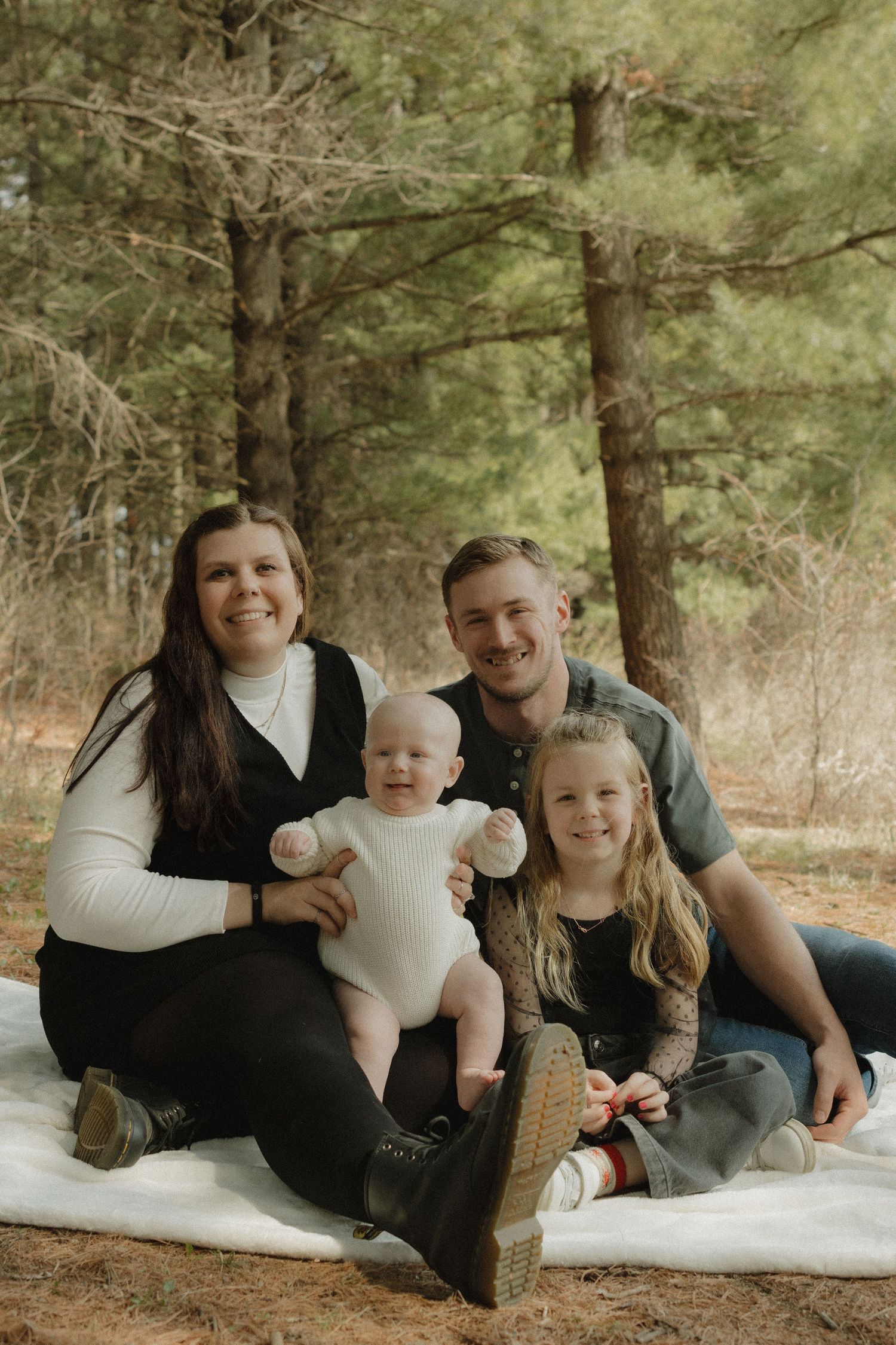 Happy family with two children poses for casual portrait in wooded outdoor setting.